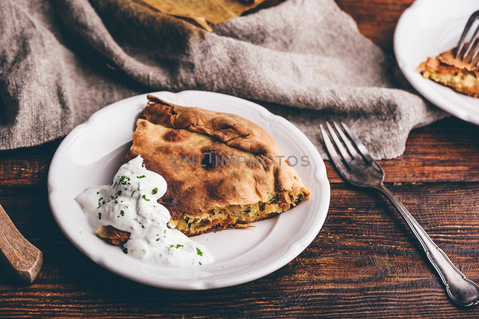 Slice of cabbage pie with sour cream sauce on white plate