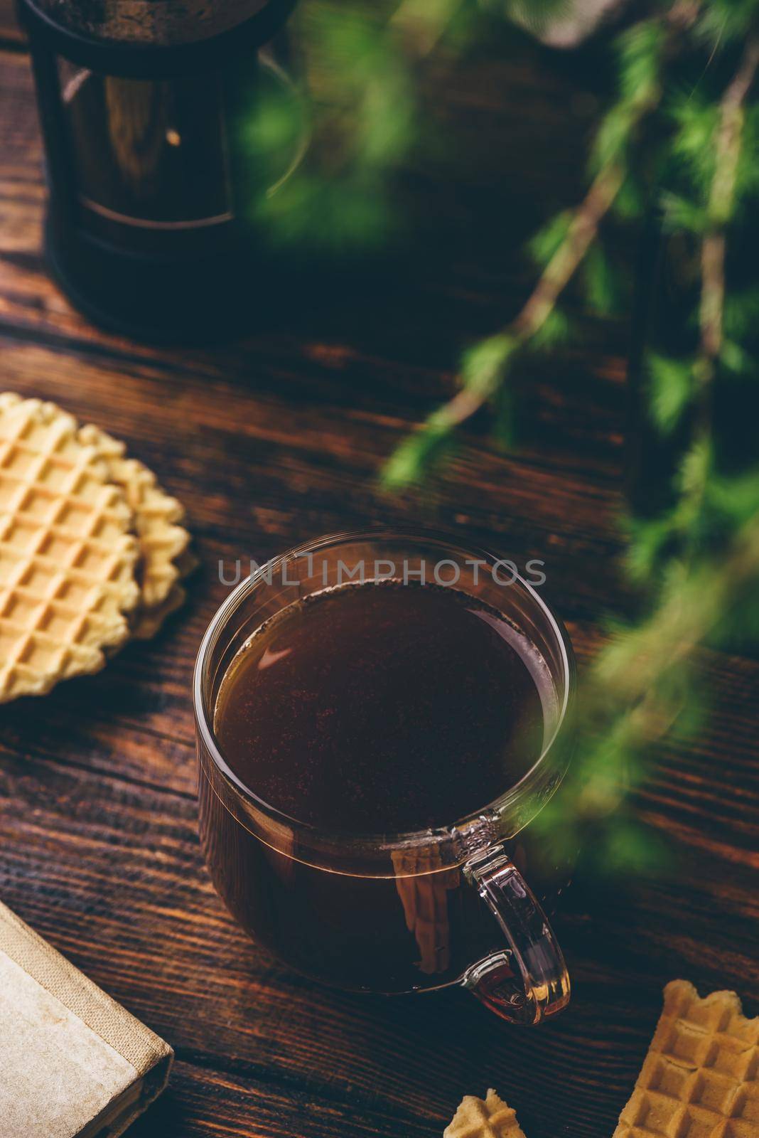 Glass cup of coffee brewed in french press with waffles on rustic wooden table. High angle view