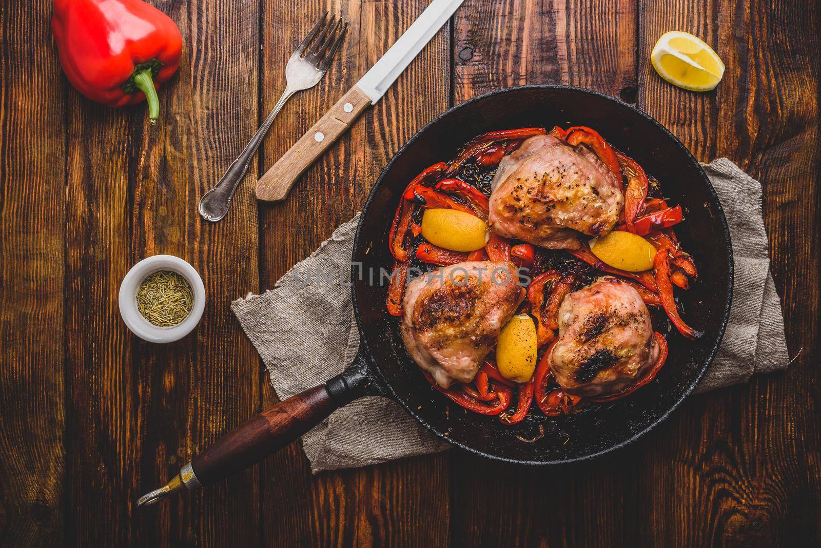 Chicken thighs baked with red bell peppers, rosemary and lemon in cast iron skillet. View from above