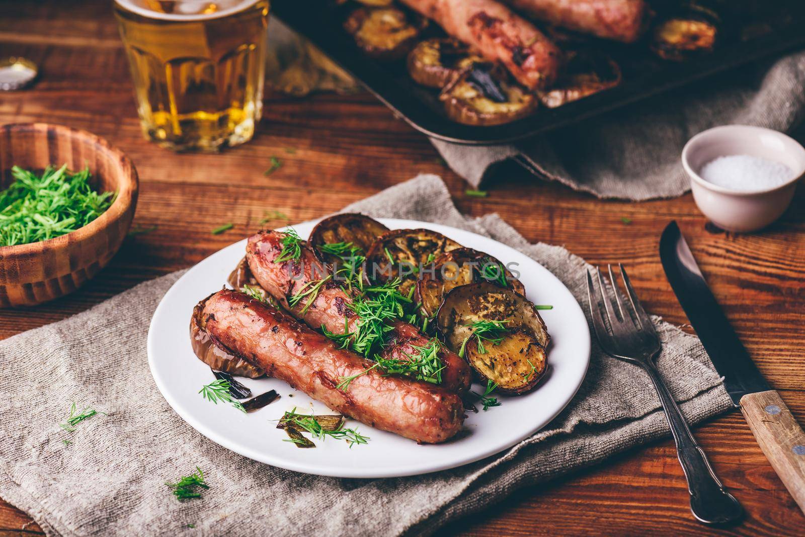 Pork Sausages Baked with Eggplant and Herbs on White Plate Garnished with Dill
