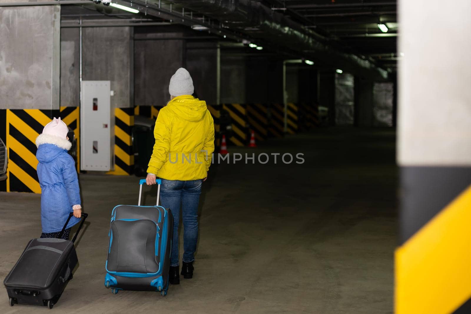 mother and daughter with luggage on wheels in underground parking