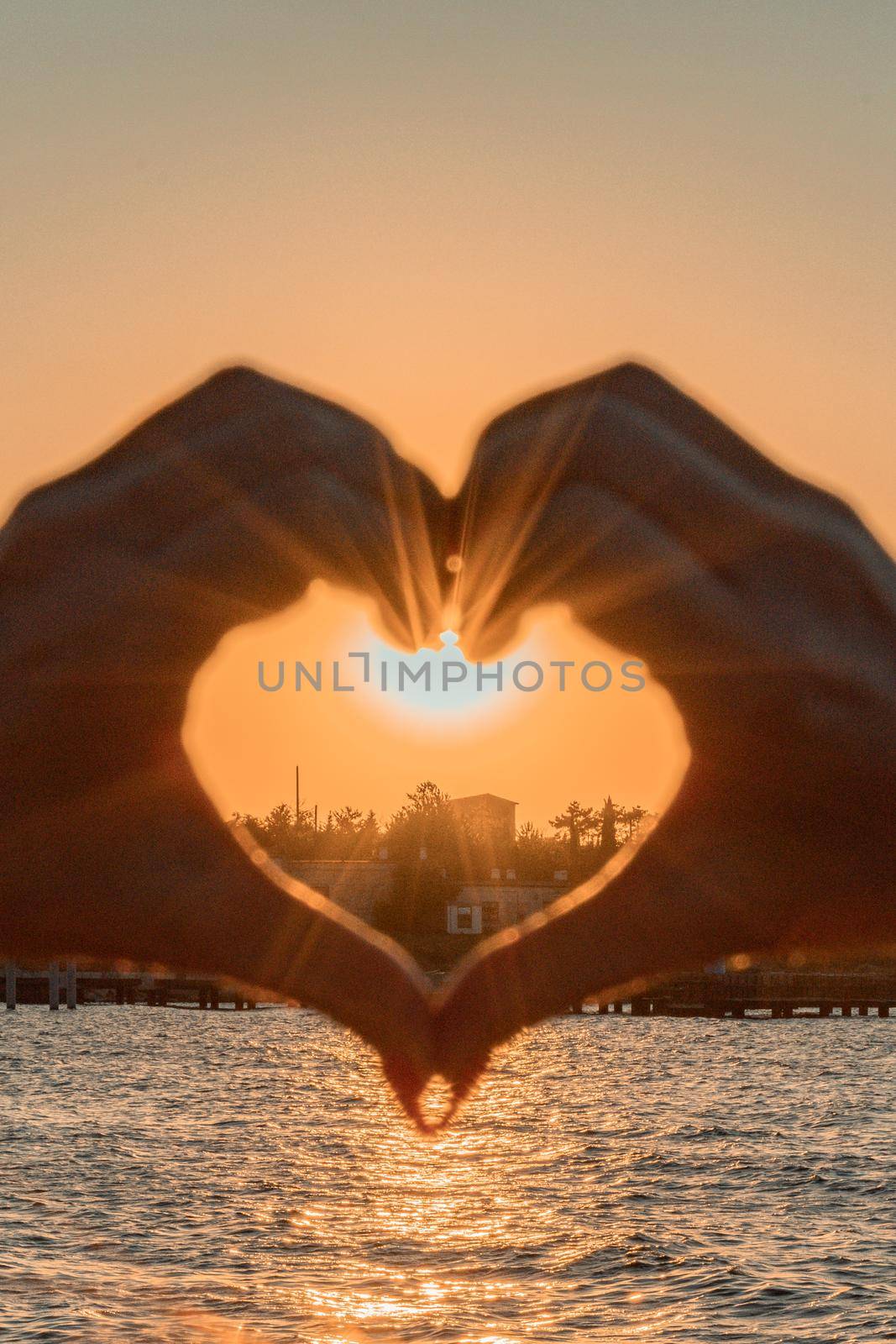 Silhouette against the sunset - hands folded in the shape of a heart. Sun with rays between the palms. Concept for Valentine's Day, declaration of love. Minimalism, space for text, warm colors