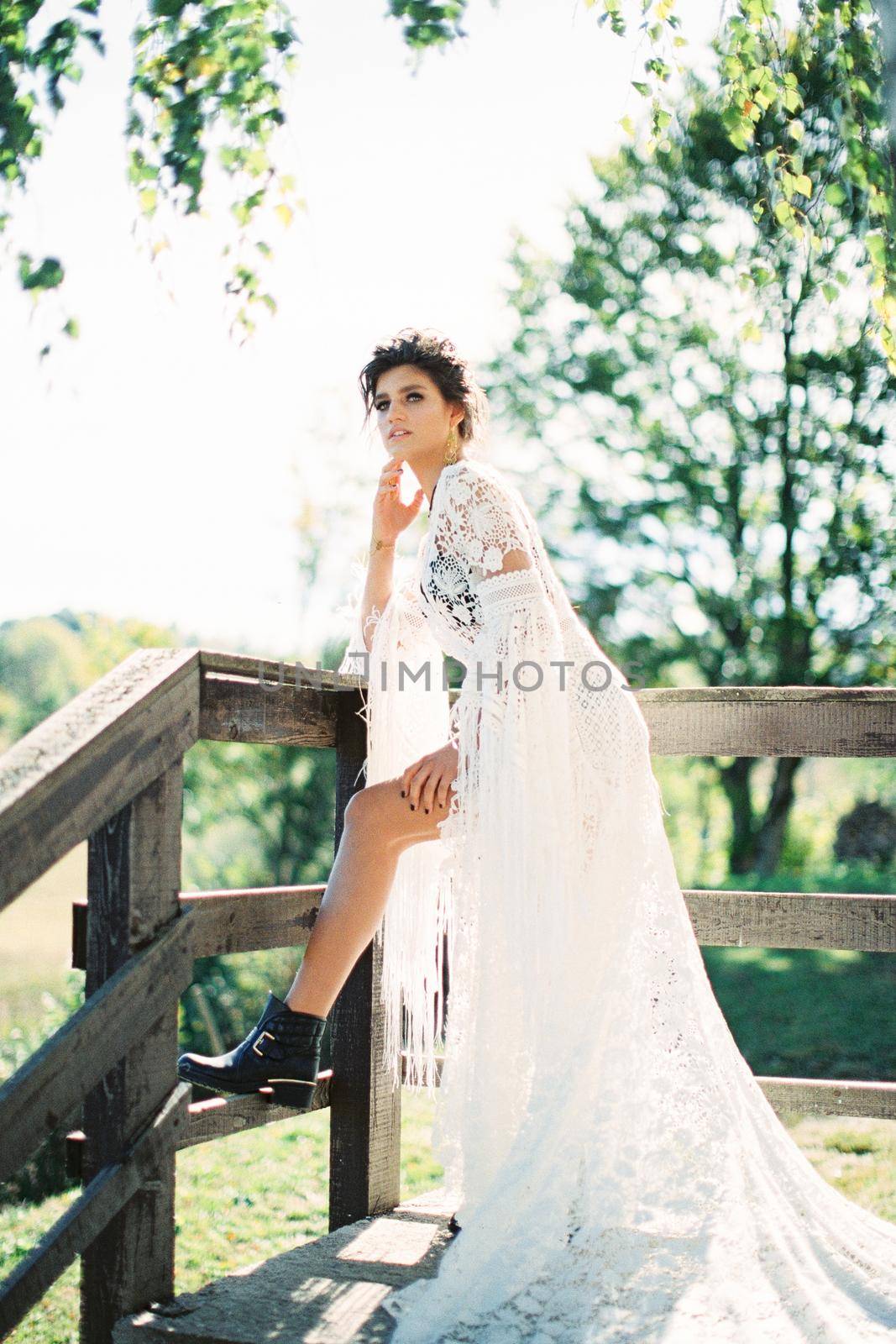 Girl in a white wicker dress stands leaning against a wooden fence. High quality photo