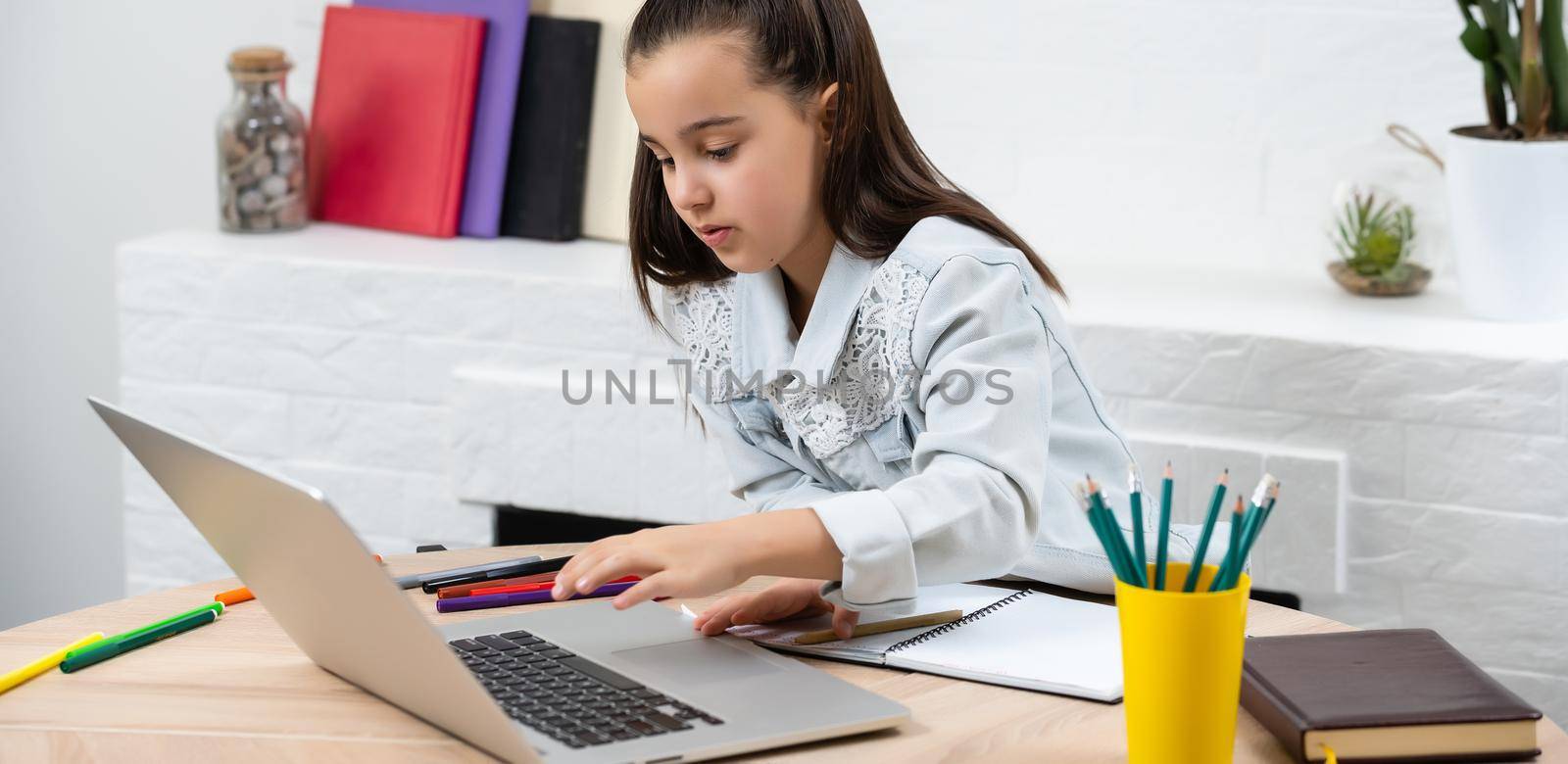 Little girl doing her homework at home and using a laptop by Andelov13
