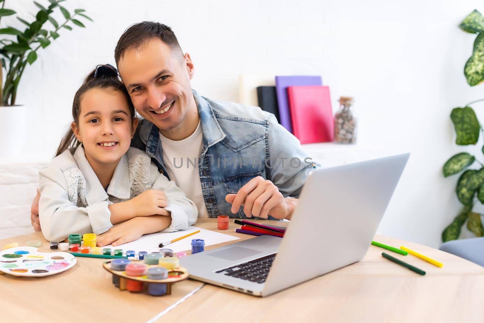 Young father helping her daughter with her school project on laptop at home by Andelov13