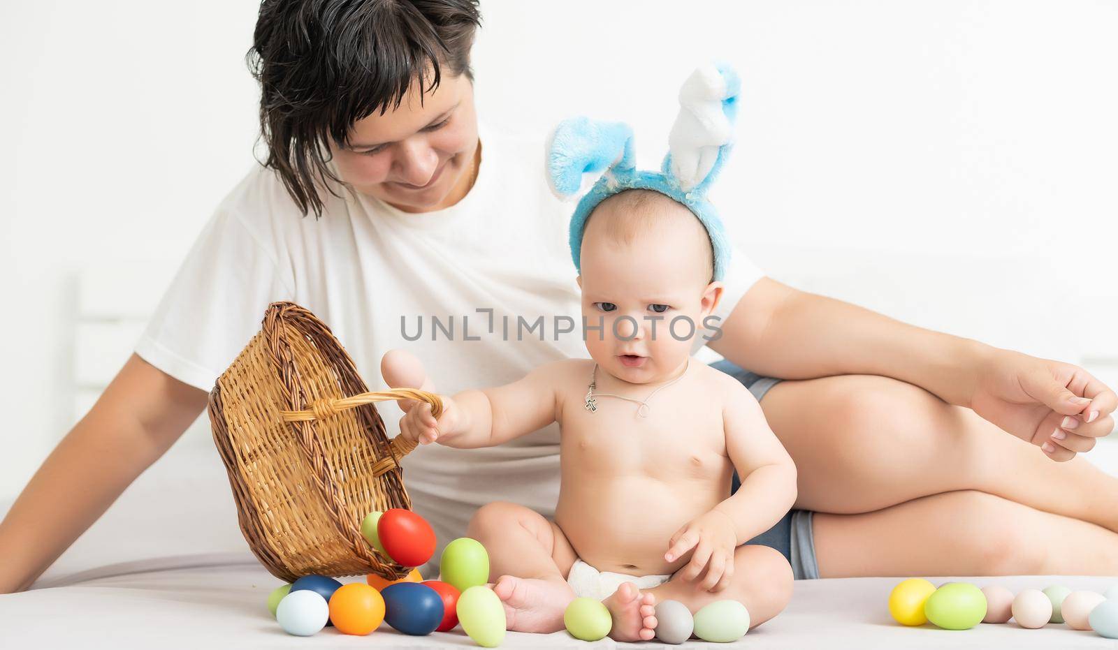 happy family celebrating easter mother and baby bunny ears at home with colorful eggs.