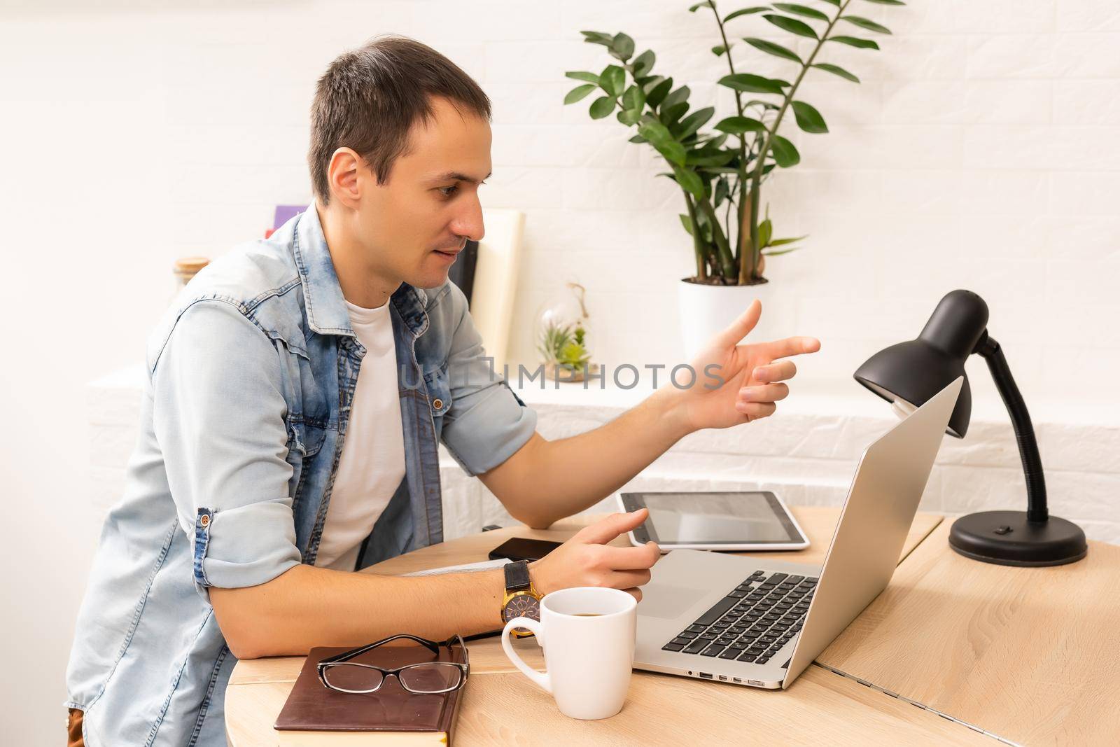 Focused young businessman holding videocall with clients on laptop. Concentrated millennial man in glasses giving online educational class lecture, consulting customer.
