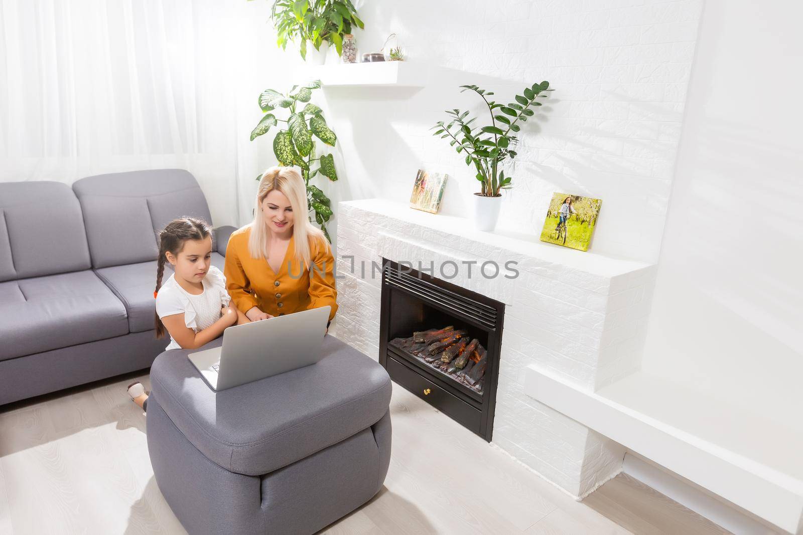 Smiling mother and toddler daughter looking at the notebook indoor. Distance online learning concept. Activities for kids during quarantine.