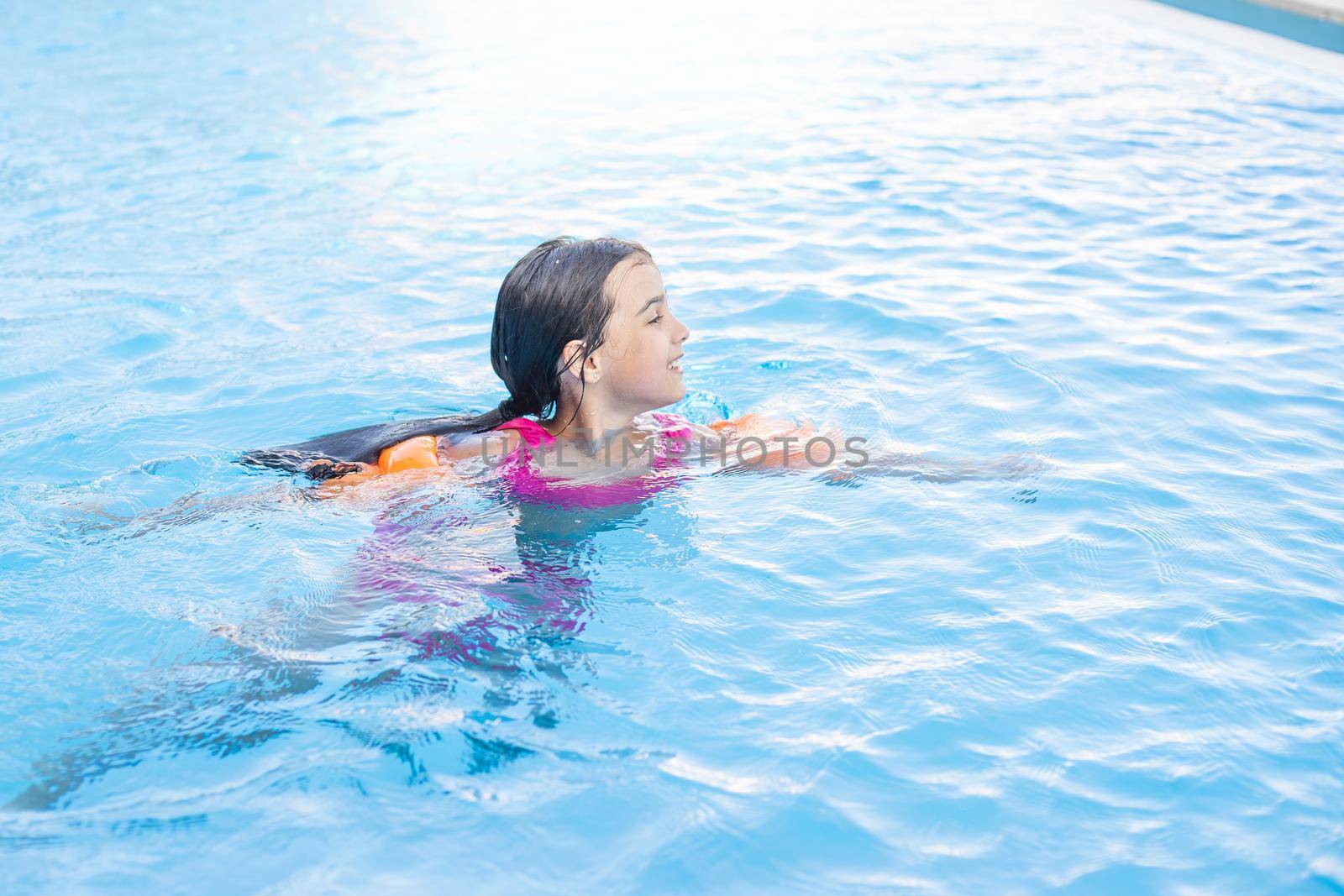 Pretty little girl swimming in outdoor pool and have a fun.