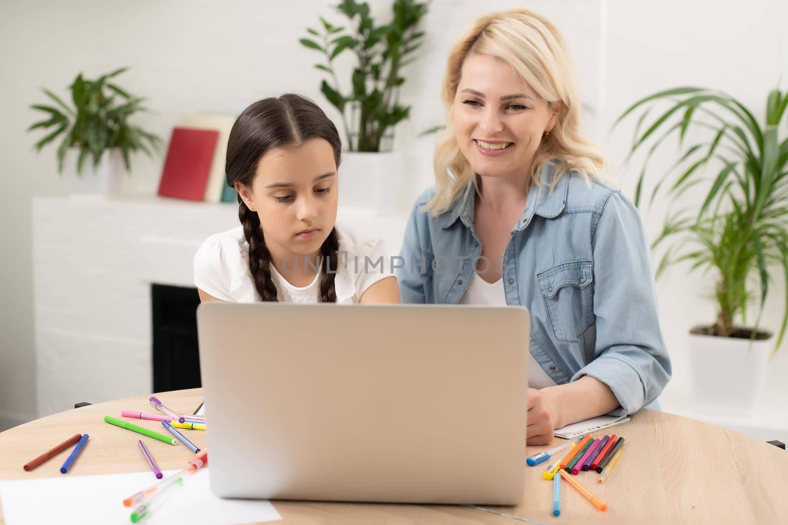 Beautiful young woman and her little cute daughter are using laptop at home. Enjoying spending time together