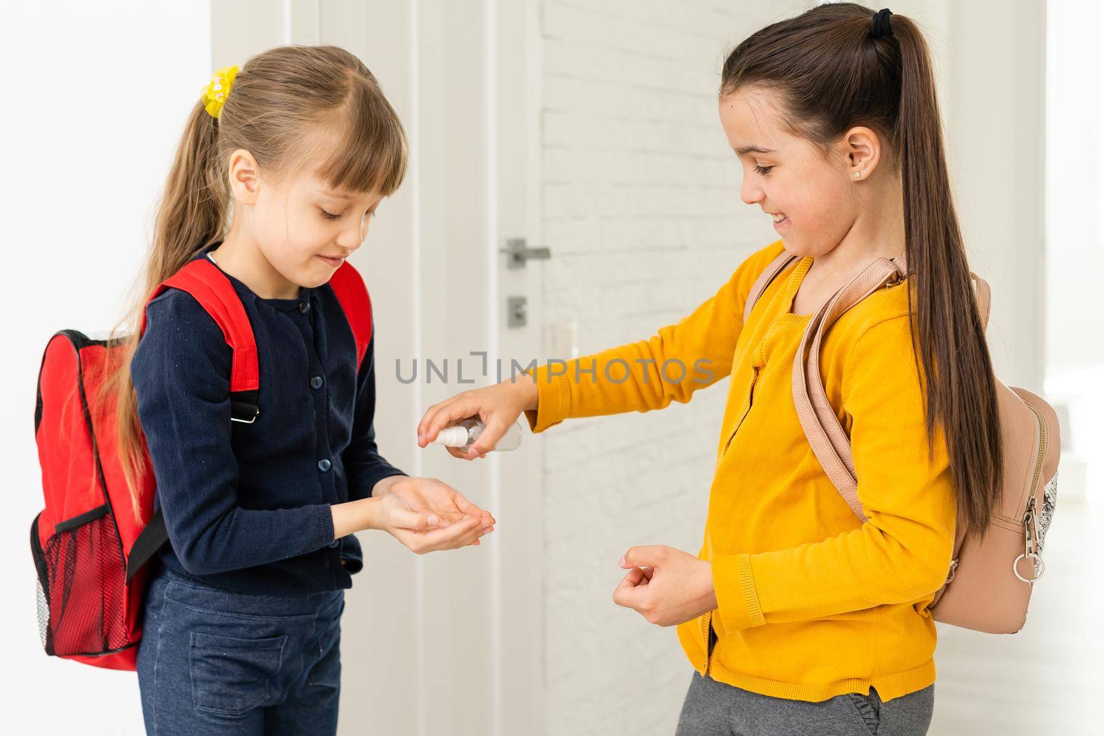 two schoolgirls applying hand sanitizer in classroom.