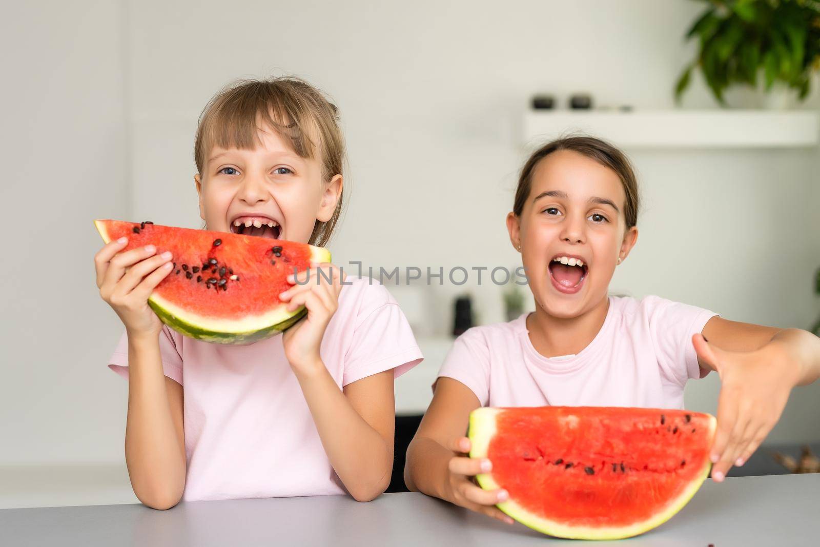 Funny little sisters eating fresh juicy watermelon at home.