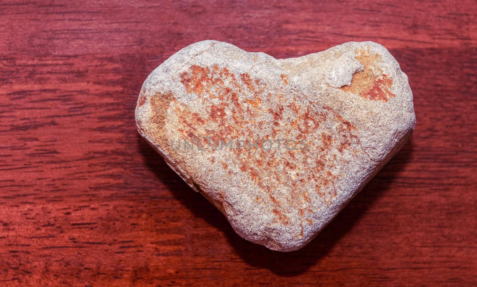 stone shaped like a heart on a wooden surface in red tone. Heart made of natural stone on a wooden background. Valentine's day and holiday concept.