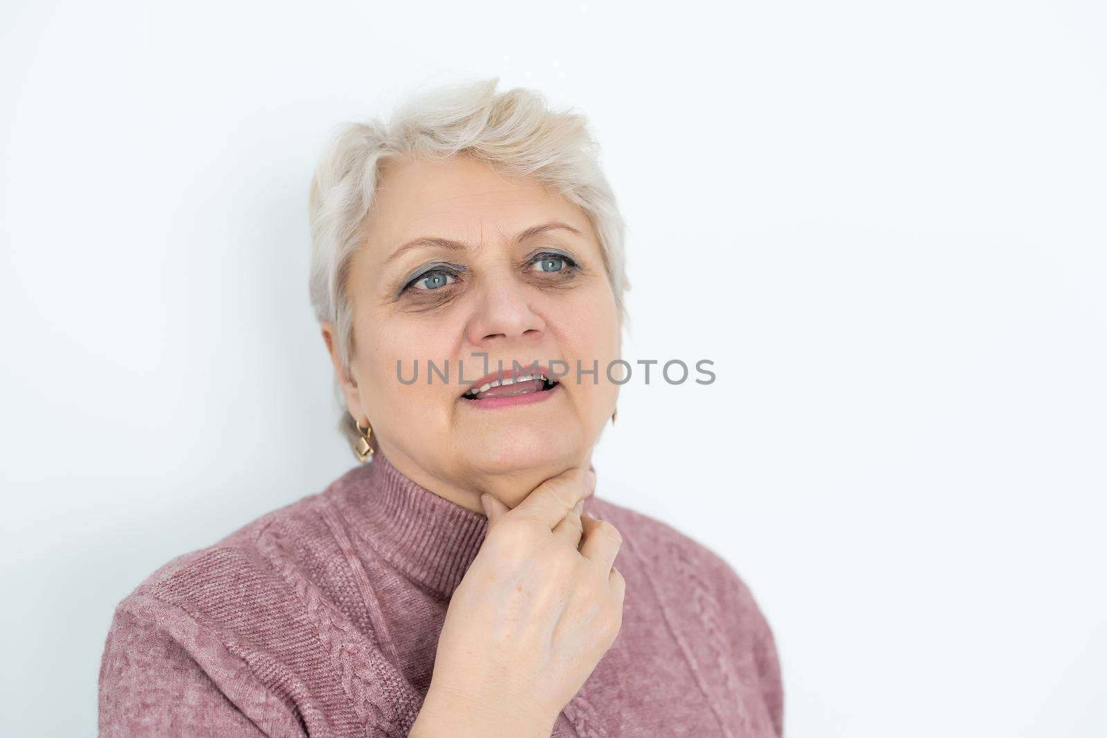 Advertisement concept. Close up profile with copy space of nice, charming, aged woman, touching her skin of neck with hand over grey background.