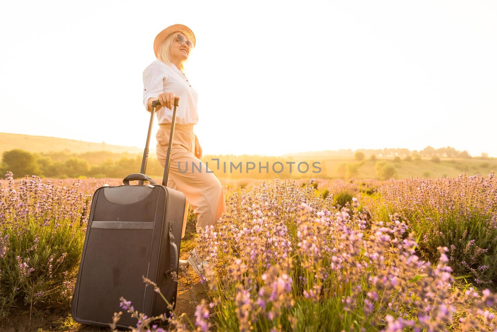 Full length portrait of pretty young lady, wearing light dress, straw hat, walking with bag in summer flowering lavender field, enjoying scent of lavender by Andelov13