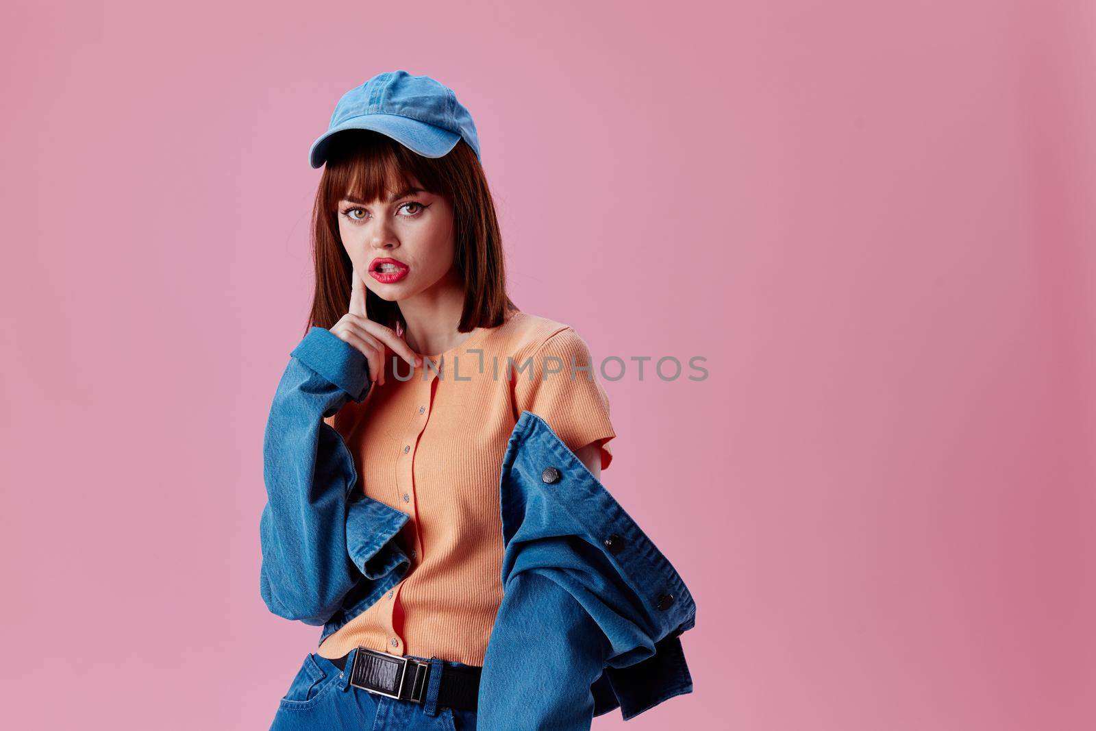 Positive young woman in a cap and denim jacket posing pink background unaltered. High quality photo