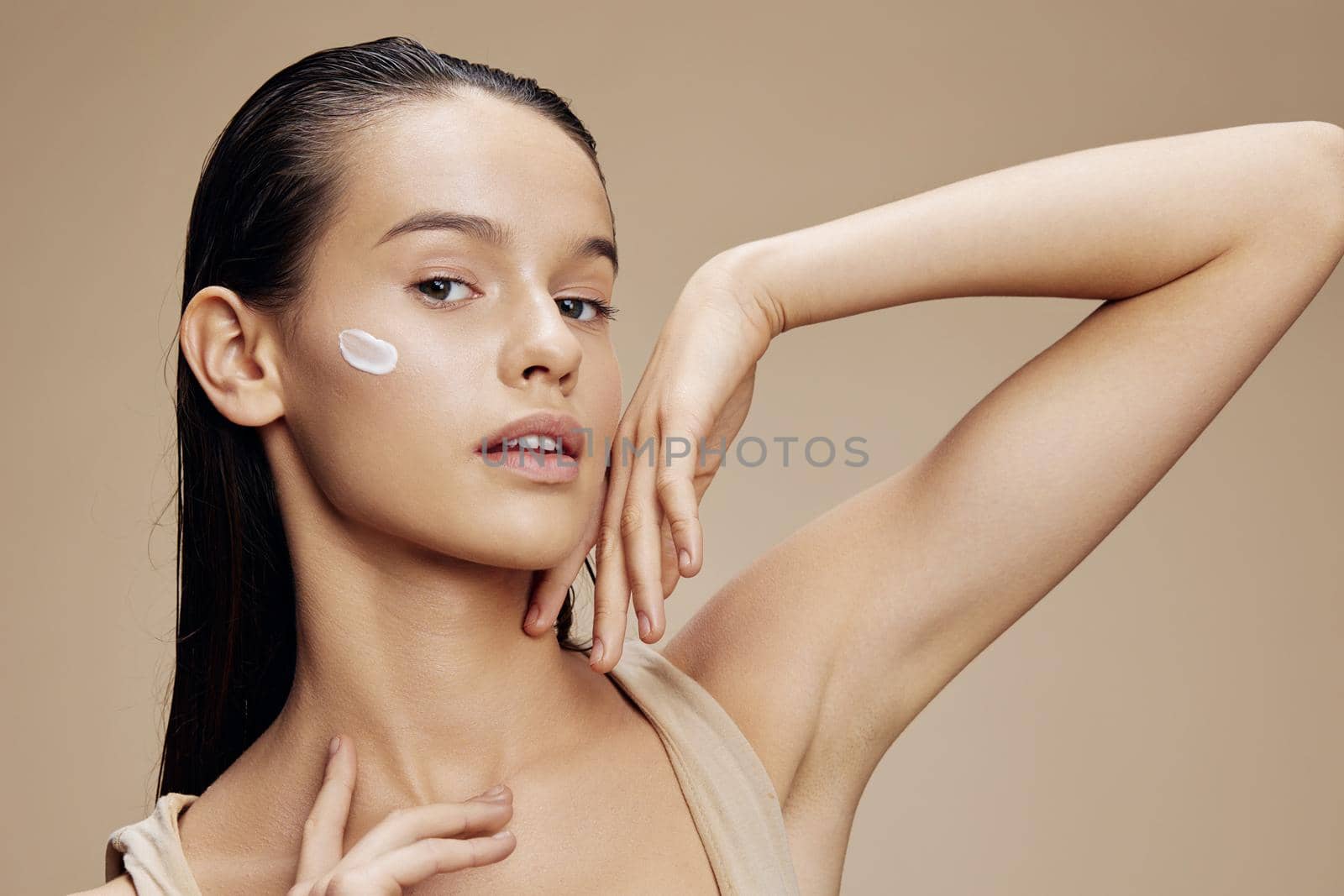 young woman applying a soothing face mask cosmetic beige background. High quality photo