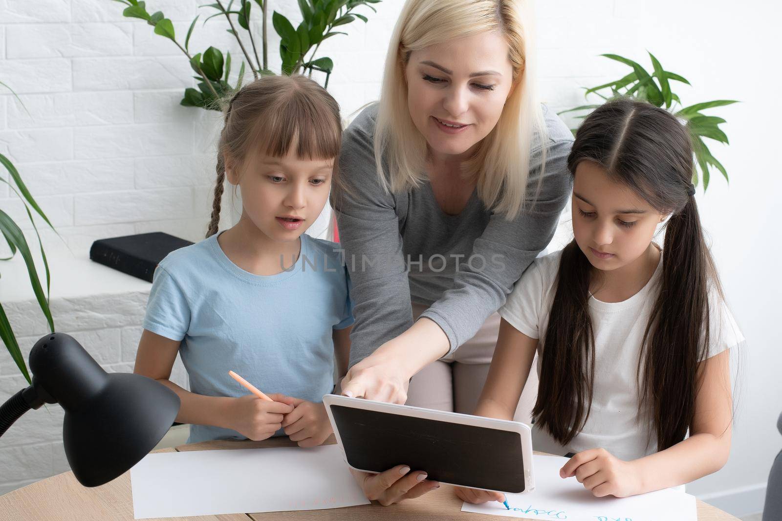 Beautiful young mother helping her daughters with homework. by Andelov13