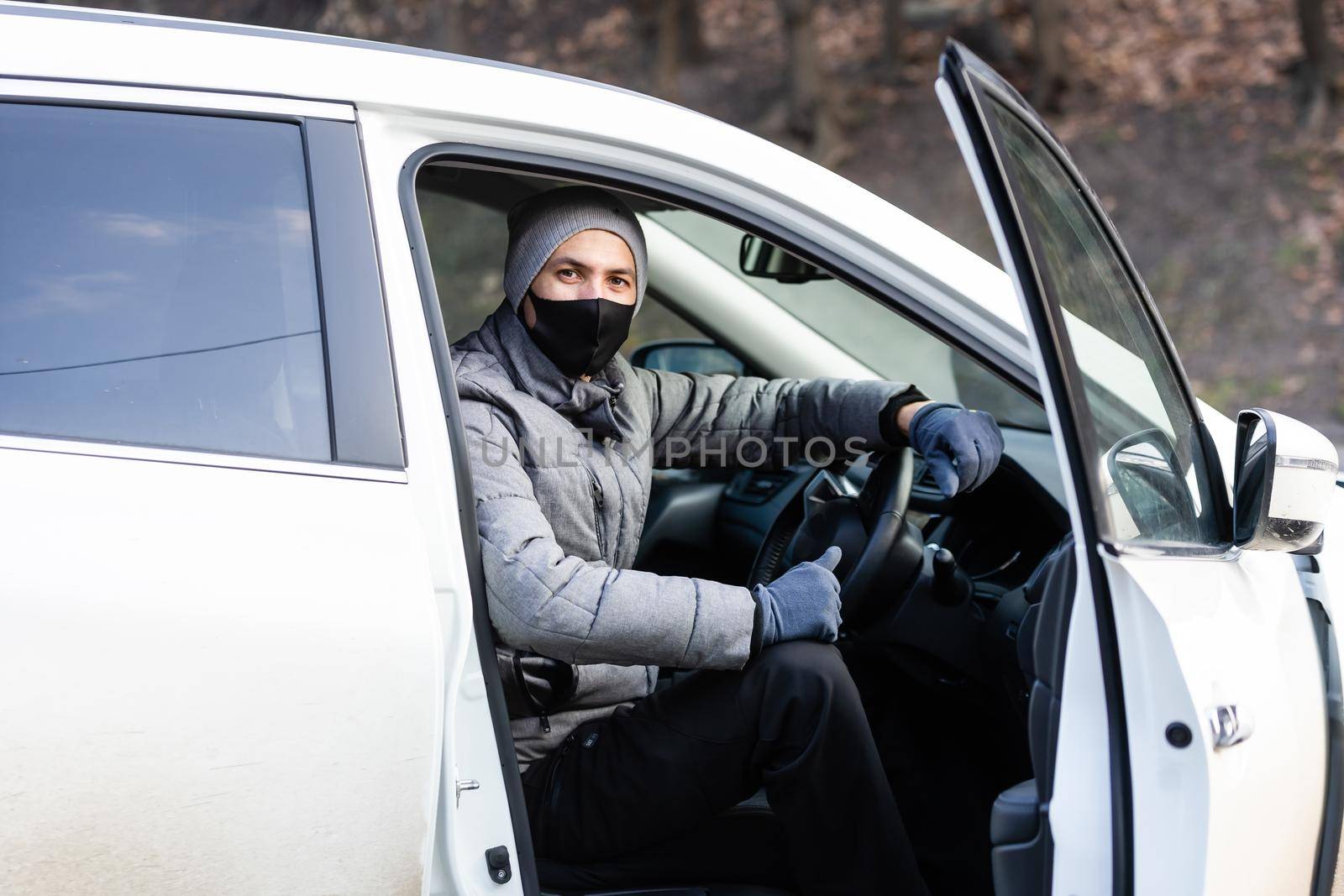 Young adult brunette man in surgical medical mask, jacket posing on city street near the car. Outdoor shot