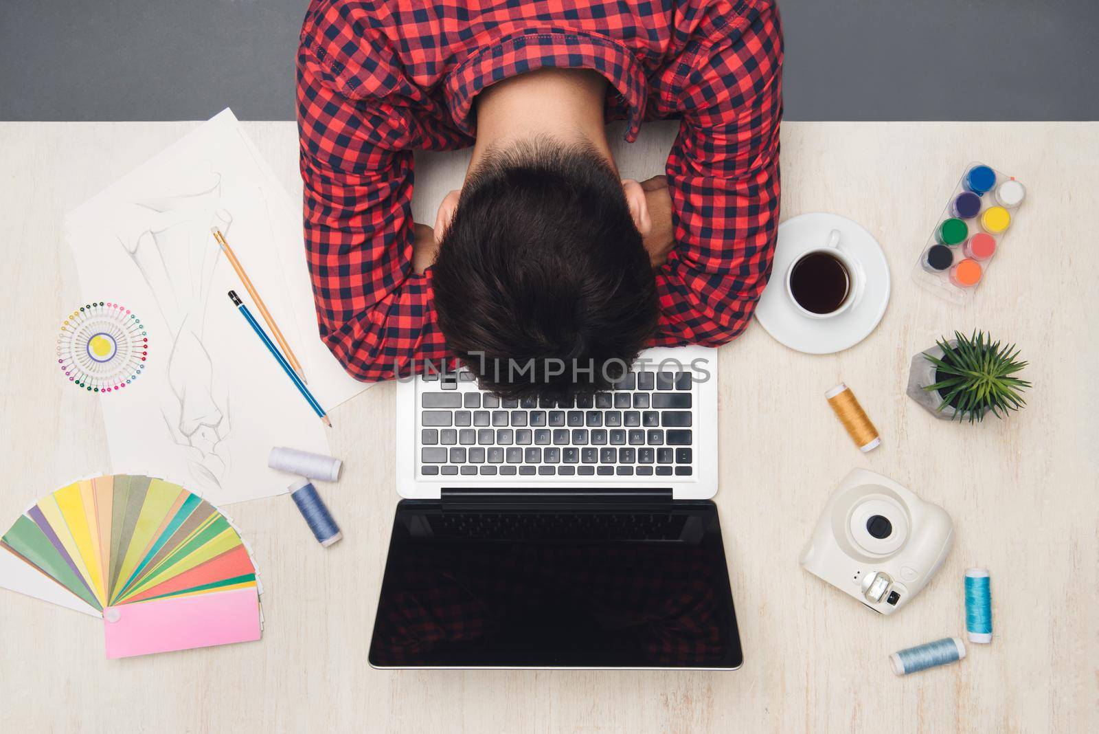 Male fashion designer is sleeping on his office table. Top view