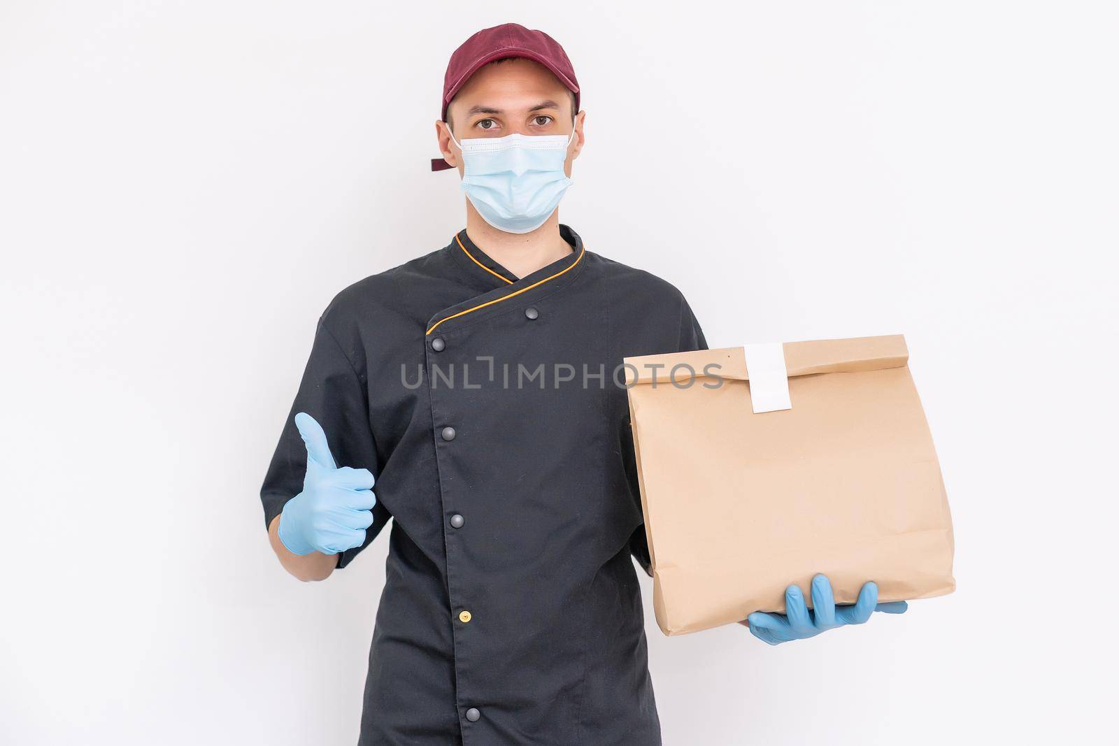 Delivery guy with protective mask and gloves holding box, bag with groceries in front of a building