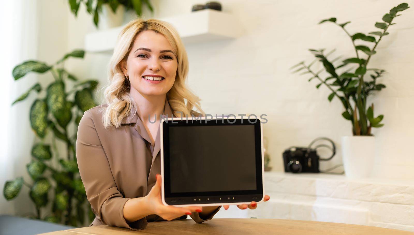 Young smiling woman showing blank tablet computer screen in office. Focus on tablet computer