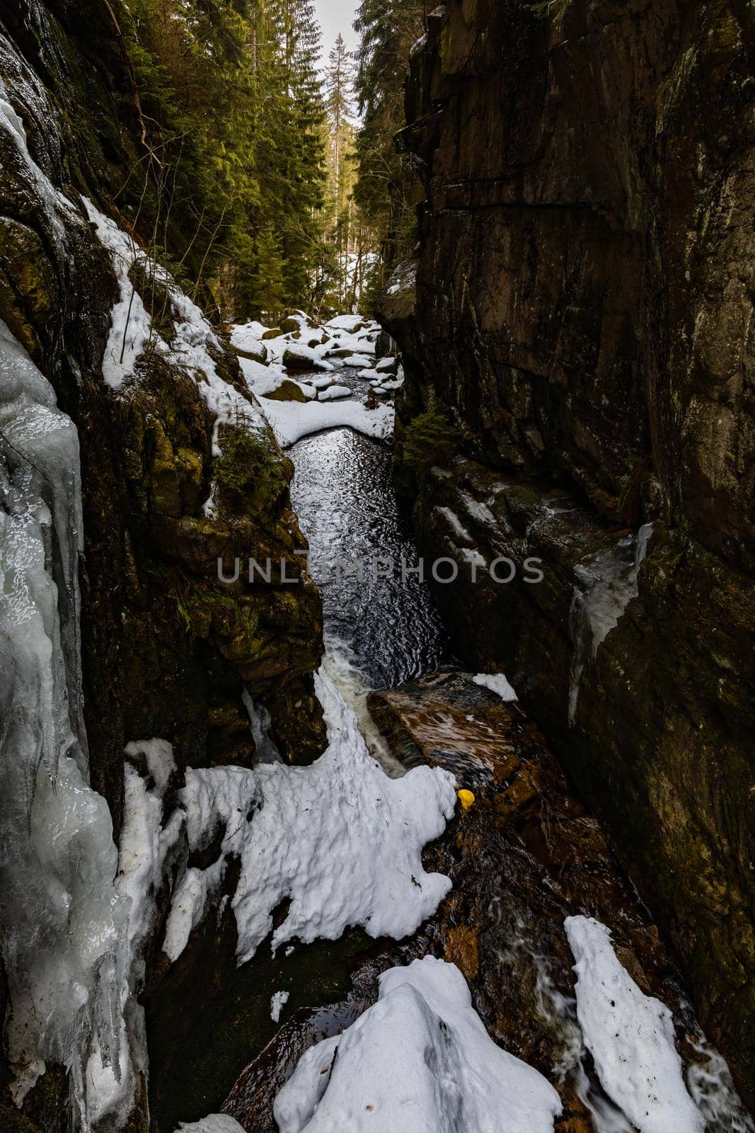 View from small footbridge over mountain river between high rocks as path to waterfall