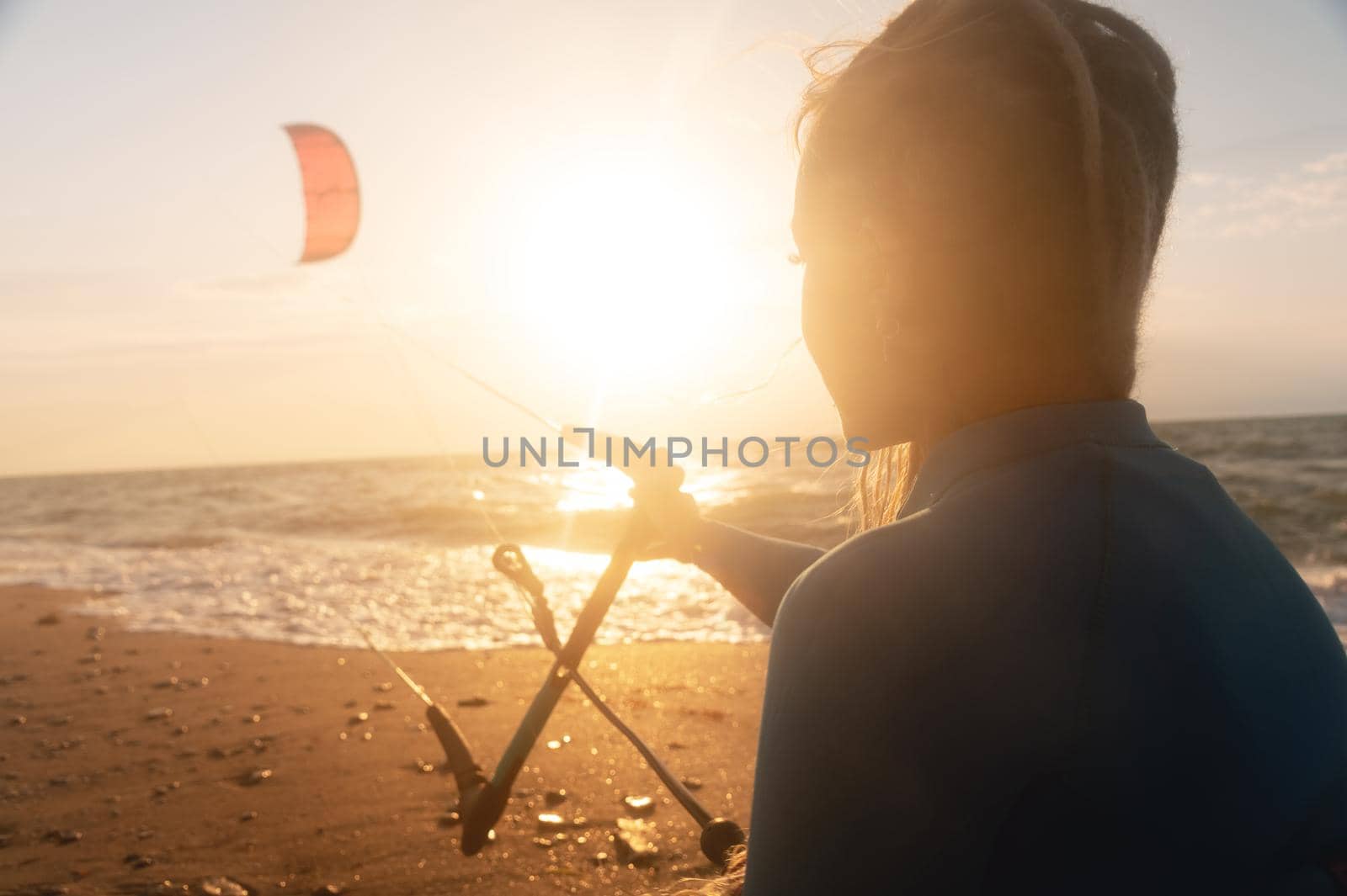 Sportswoman woman kitesurfer holds her kite over the surface of the sea with waves at sunset. Space to copy water sports. Kitesurf instructor looking at the setting sun and kite by yanik88