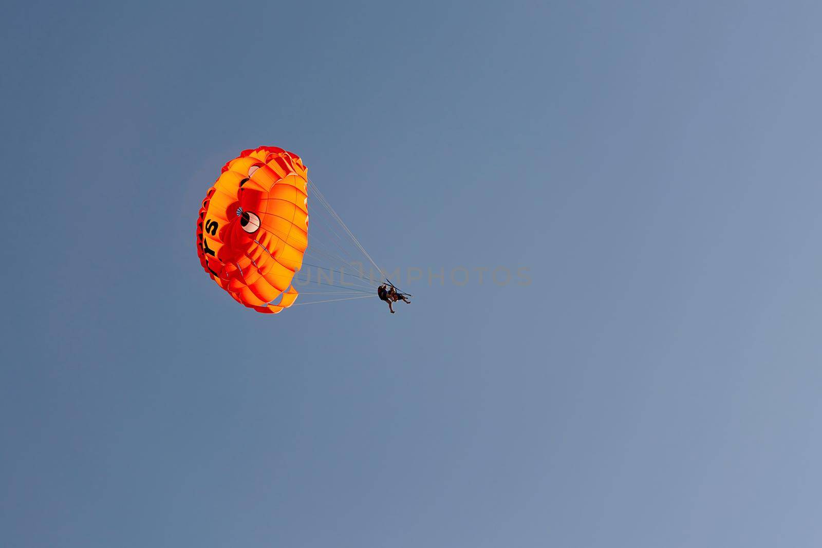 Parachute with flying man against blue sky background. Extreme vacation by the sea