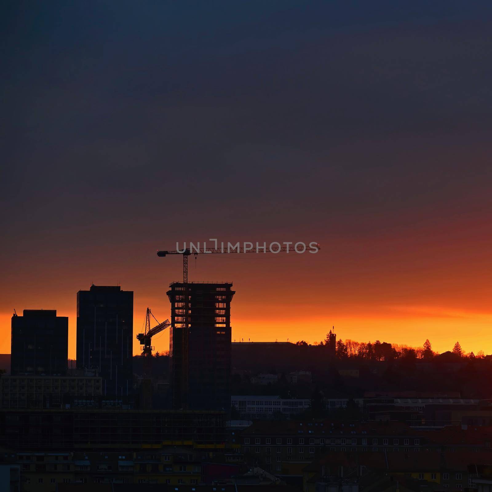 Construction of buildings with a crane, workers and construction machinery at sunset. Concept for construction and industry. by Montypeter