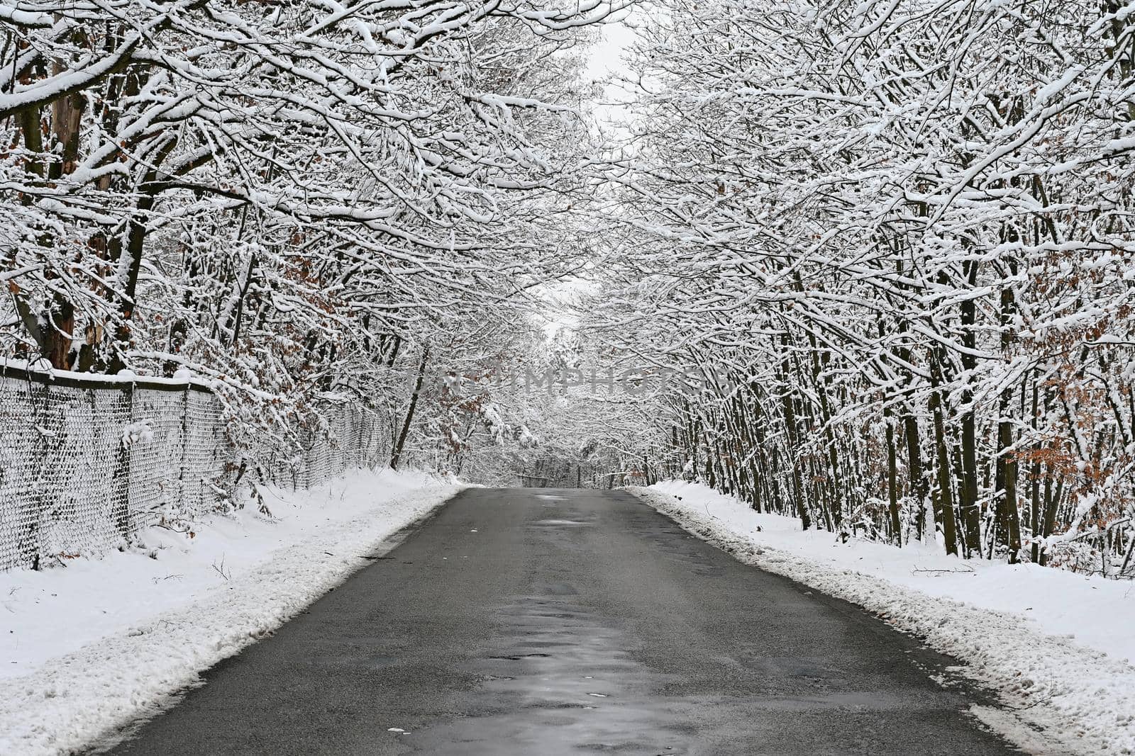 Broken, repaired poor quality asphalt road in winter with snow and icicles. Concept for transport and travel in bad winter weather.