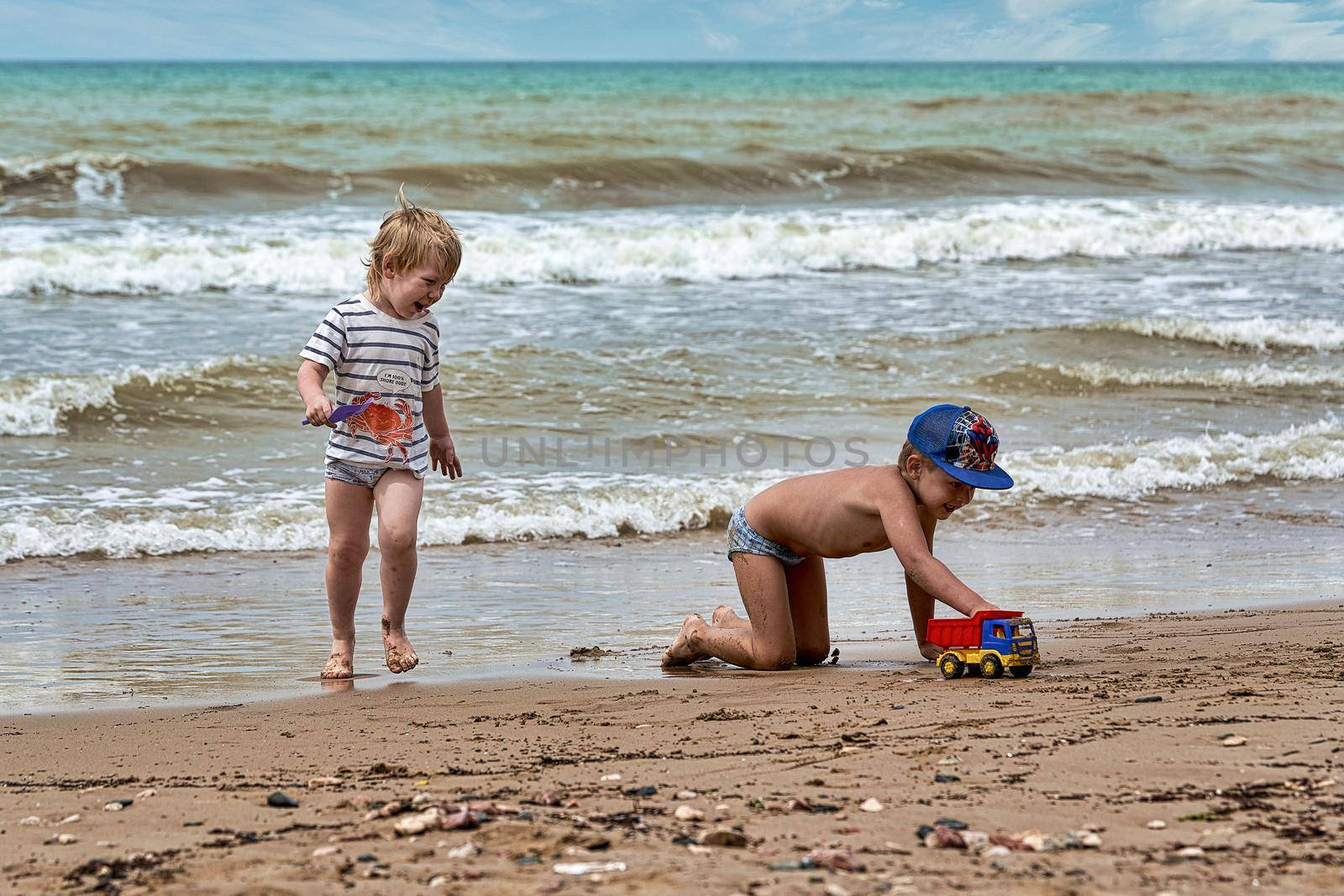 Two little boys are playing on the seashore. Children playing on the beach