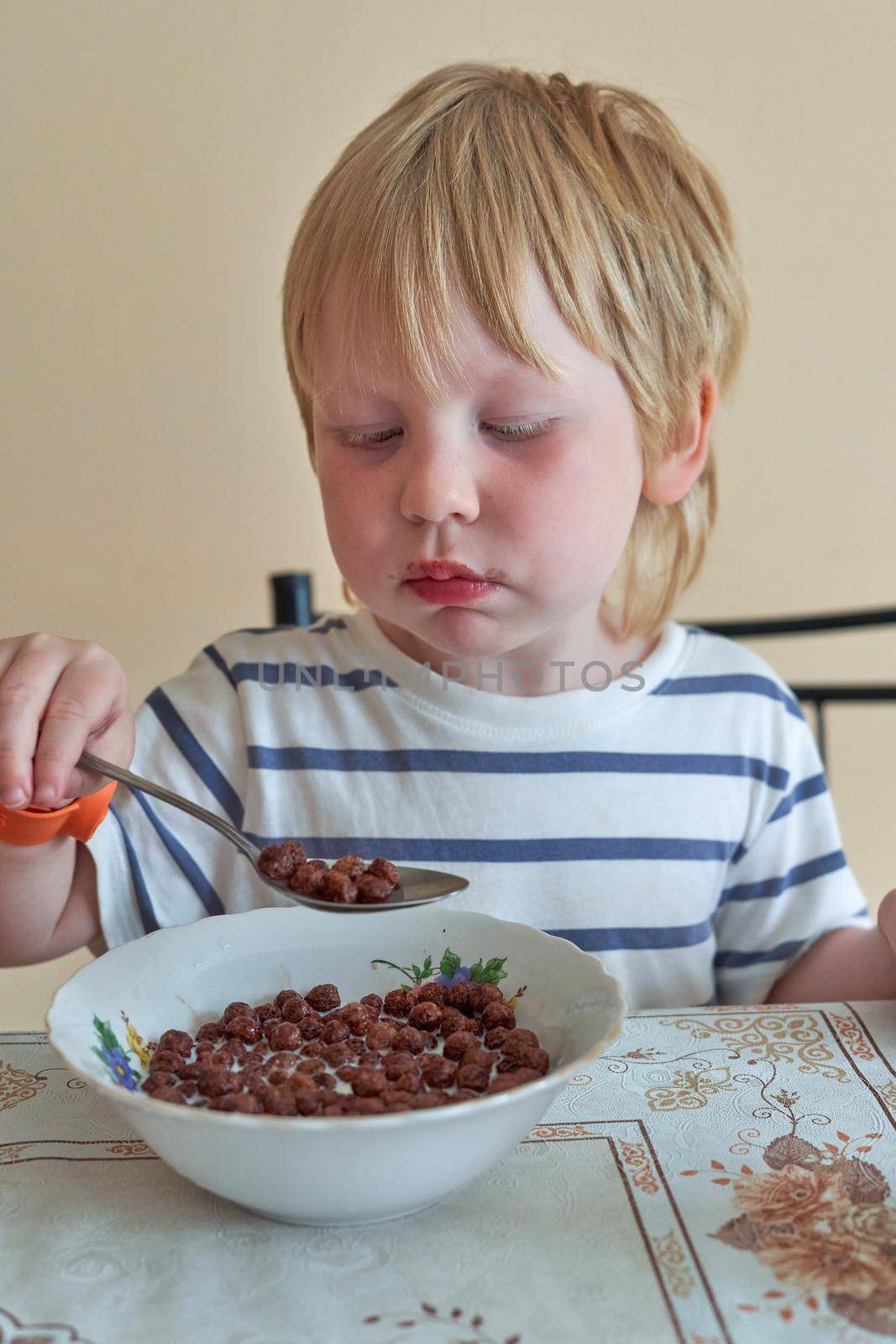 Little boy is having breakfast with chocolate balls with milk. Child eats dry breakfast with milk