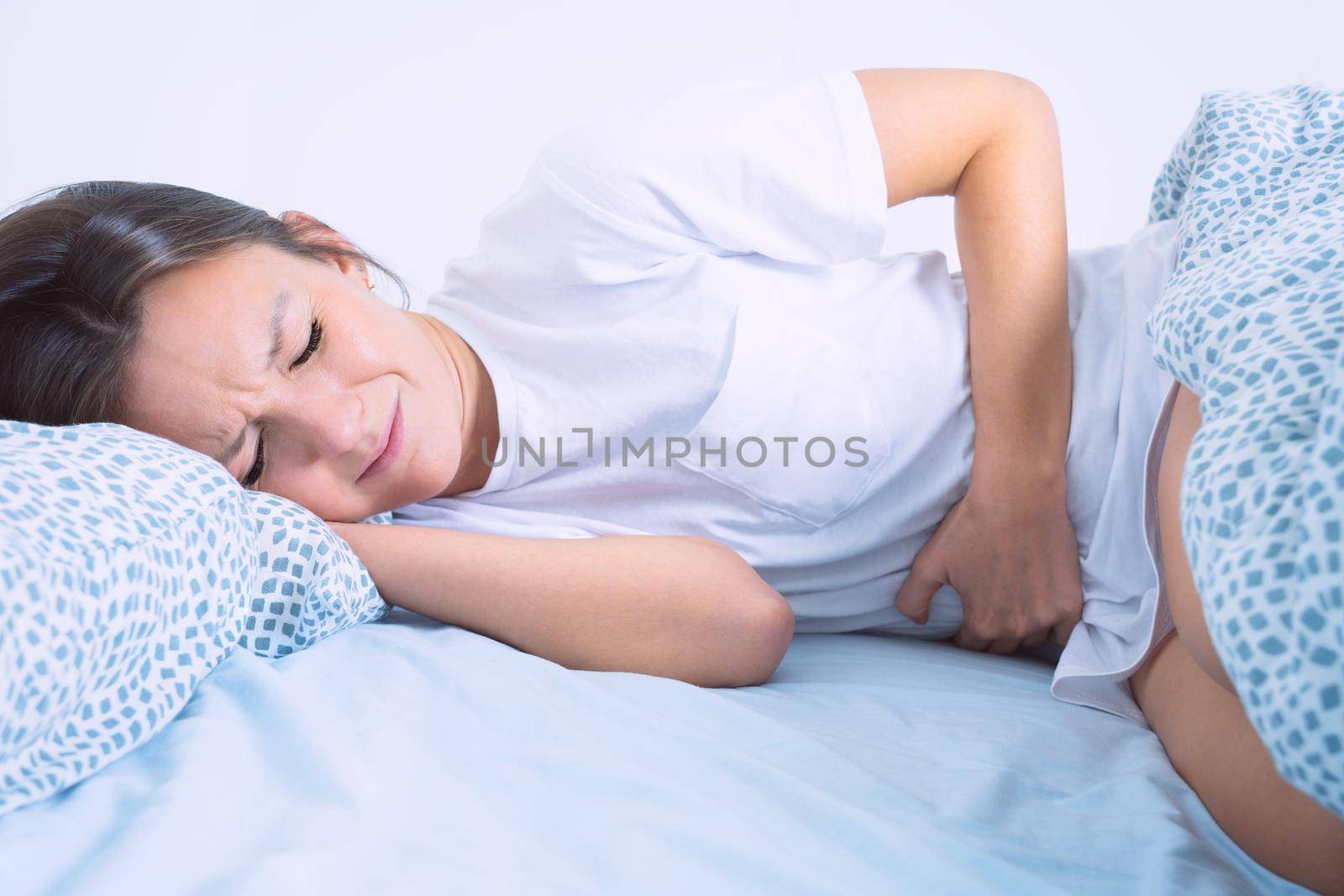 Woman in bed suffering from menstruation pain, stomach ache or abdominal pain. Menstruation period or PMS. High quality photo