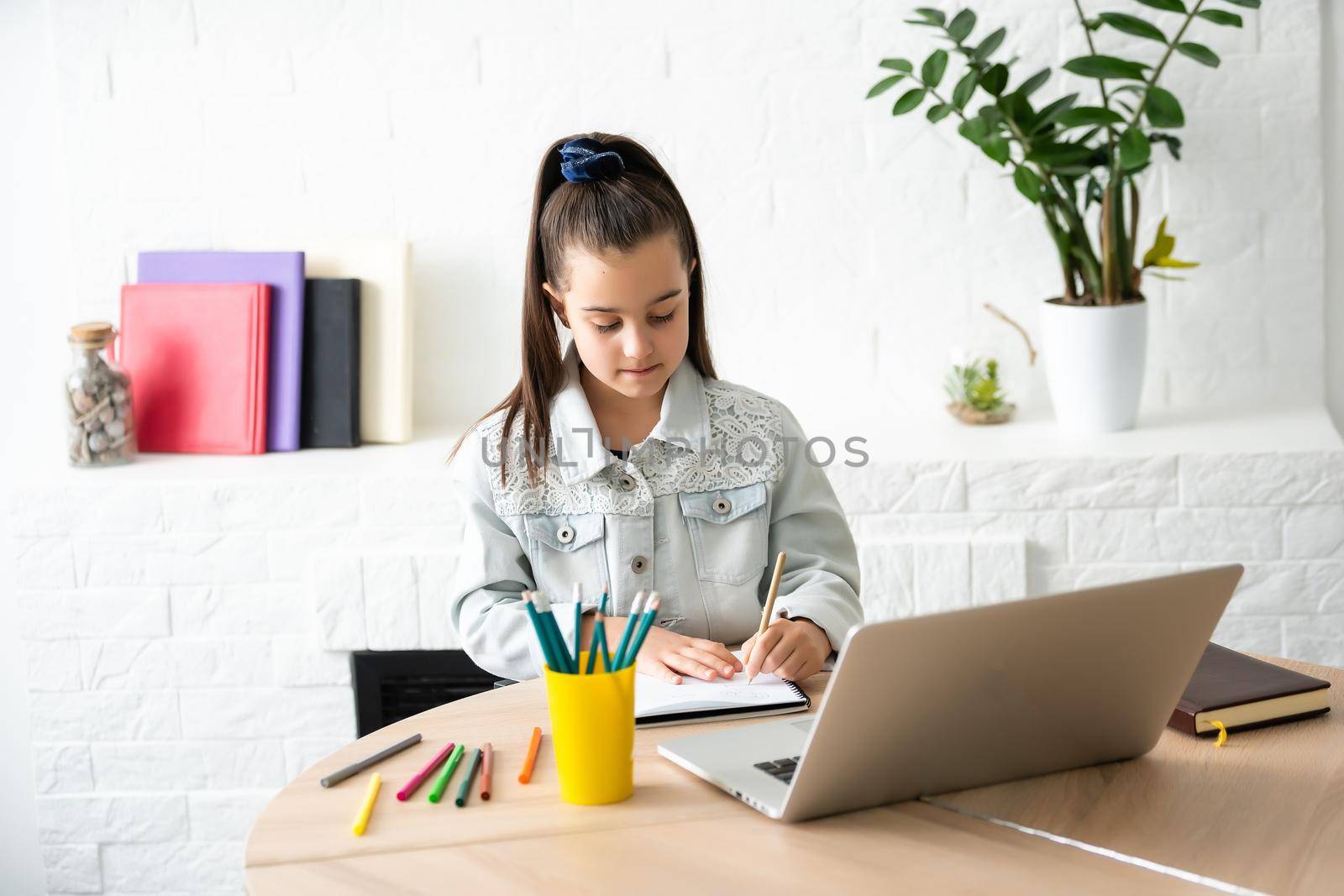 Little girl doing her homework at home and using a laptop