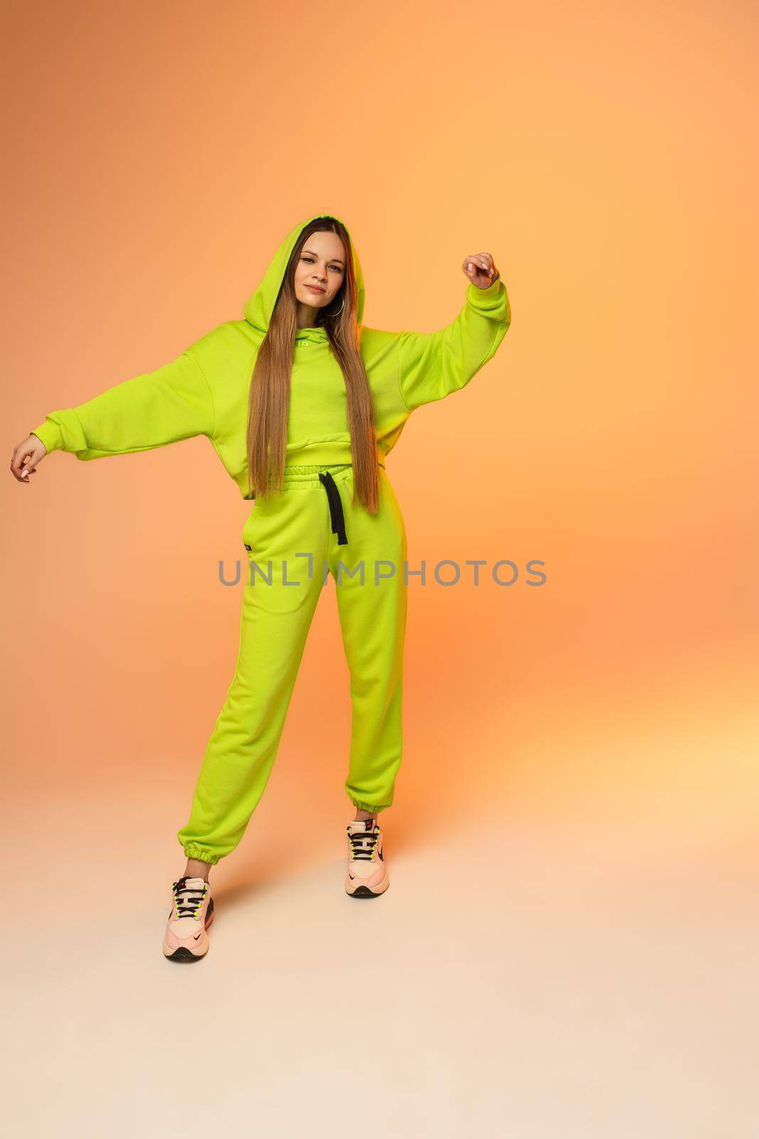 Full length photo of beautiful young woman with bright sportwear posing on orange background