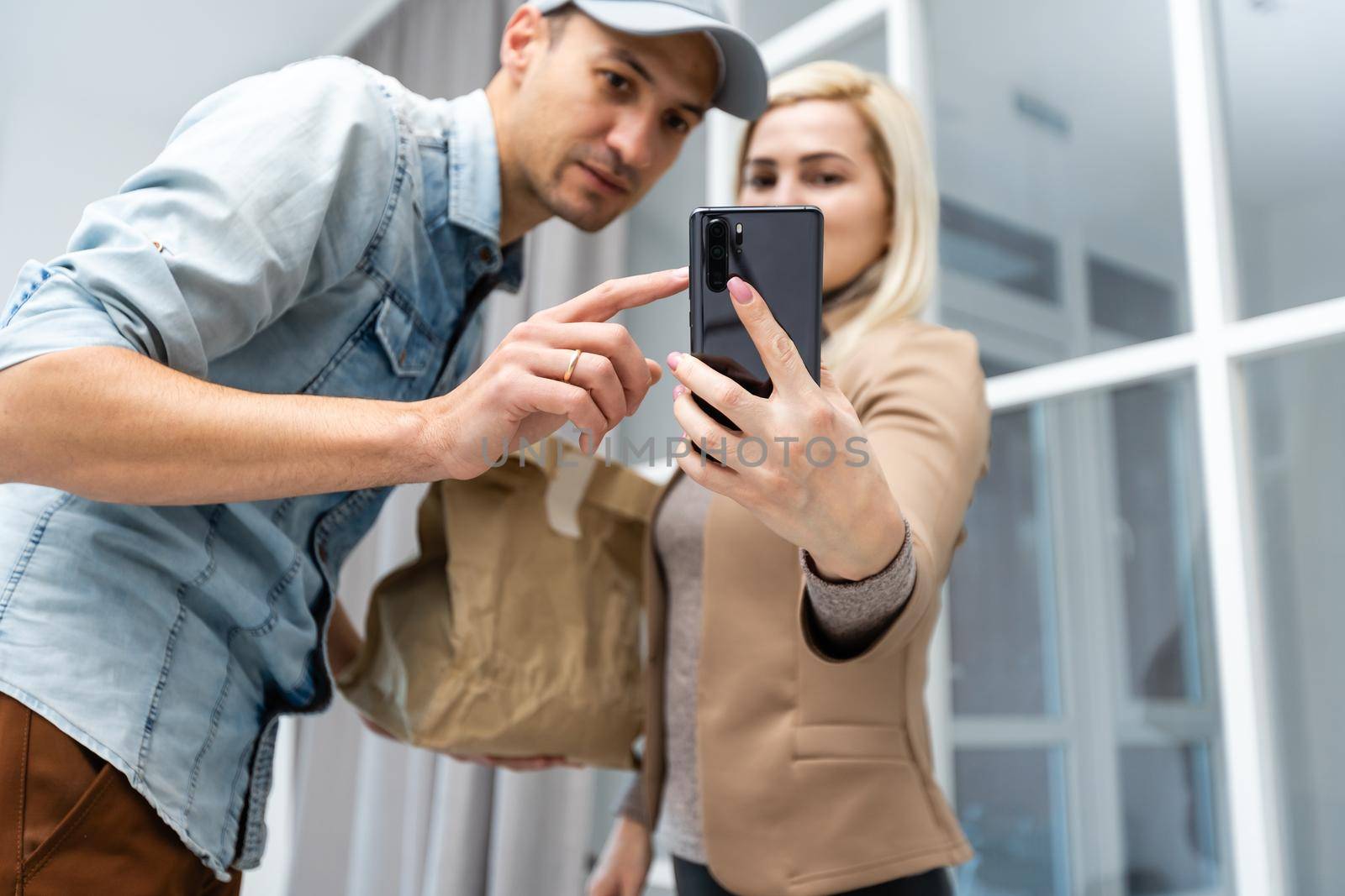 Fast and reliable service. Cheerful young delivery man giving a cardboard box to young woman while standing at the entrance of her apartment by Andelov13