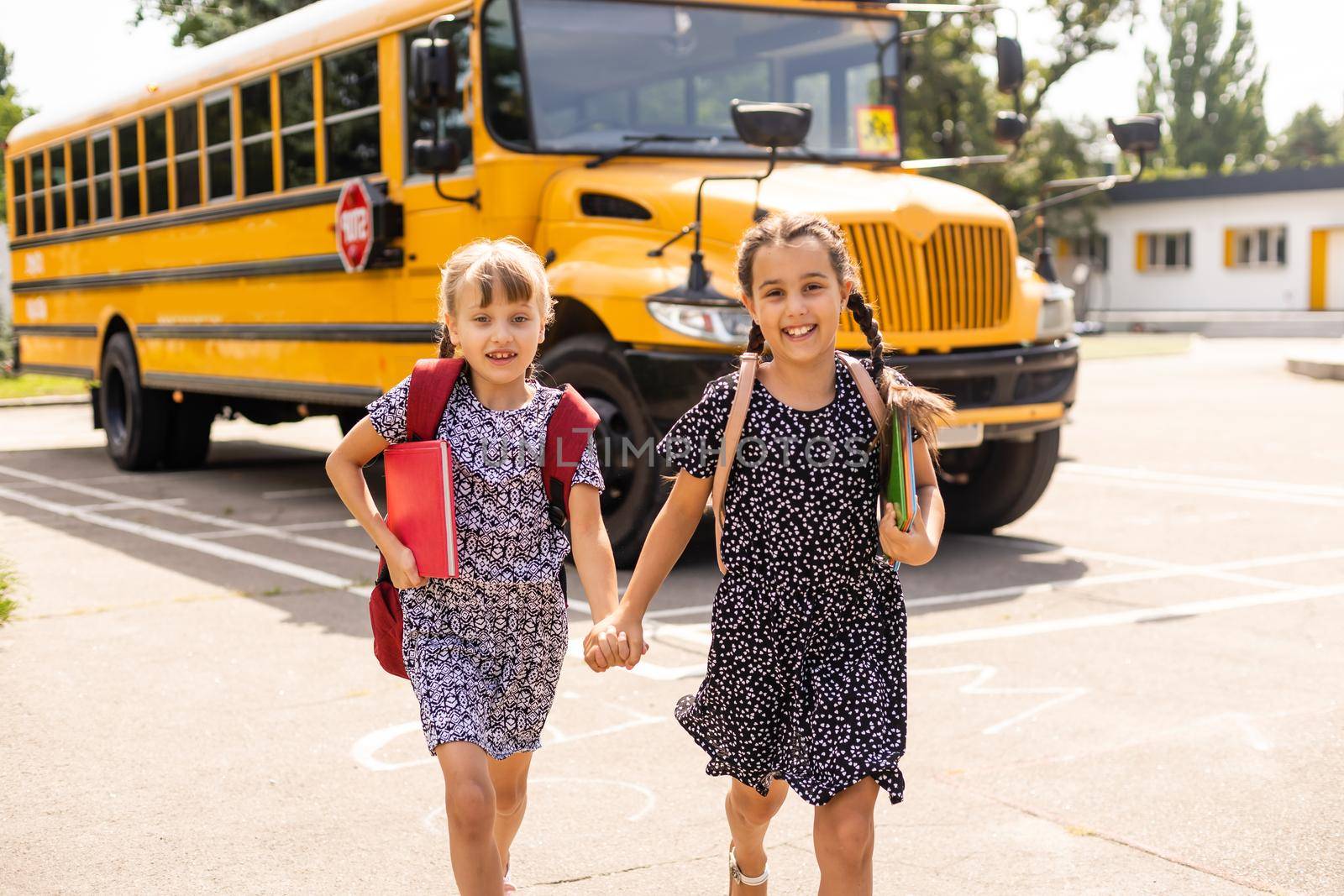 Cheerful little girls next to school bus. Backback. Back to school concept