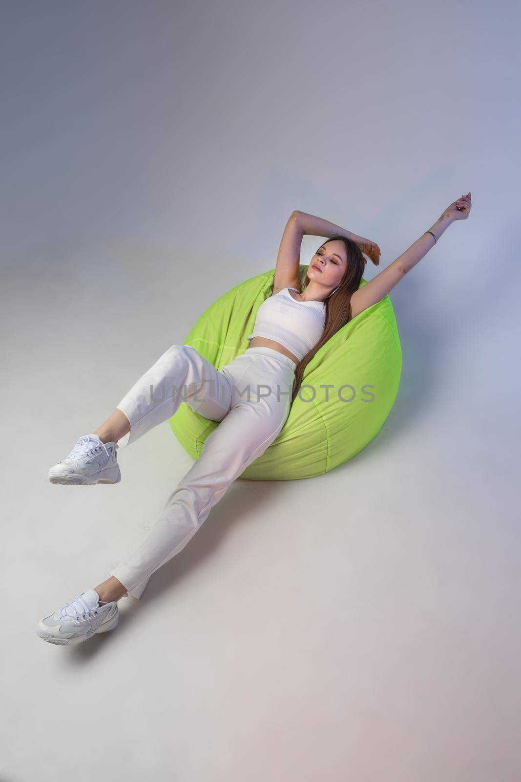 Young caucasian woman with cute face poses for the camera on a green bag chair by StudioLucky