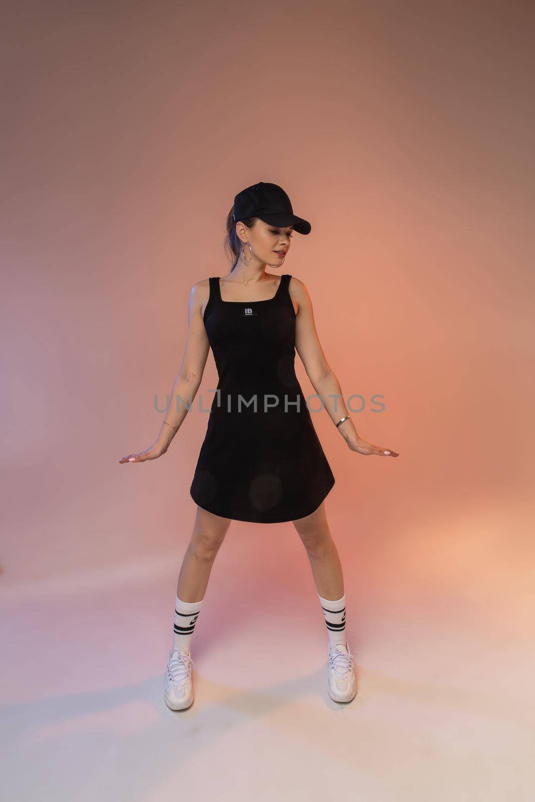 Stylish young girl female fashion model wearing sportive outfit, cool black sundress and cap posing in studio by StudioLucky