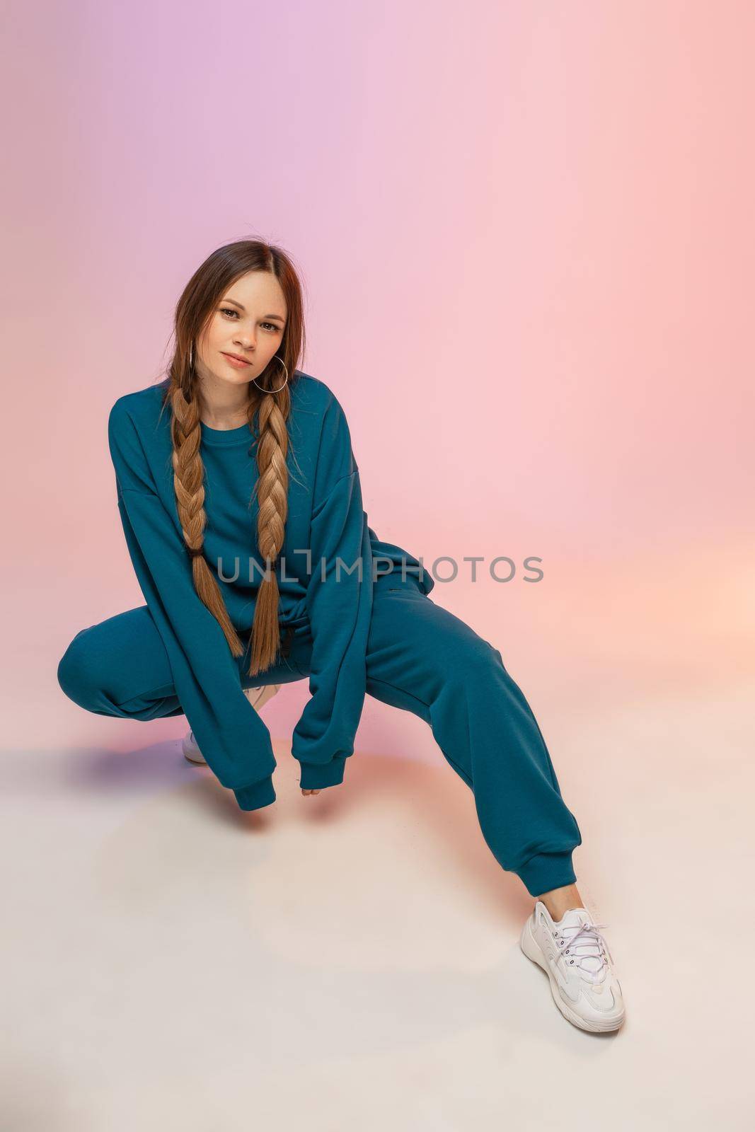 Smiling young pretty lady in suit squatting on leg and looking at the camera in studio. Copy space
