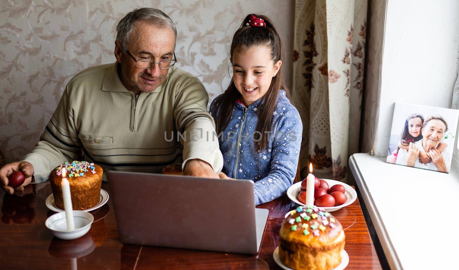 grandfather and granddaughter using laptop on kitchen, online, video call to friends, easter at home during coronavirus covid-19 outbreak. by Andelov13