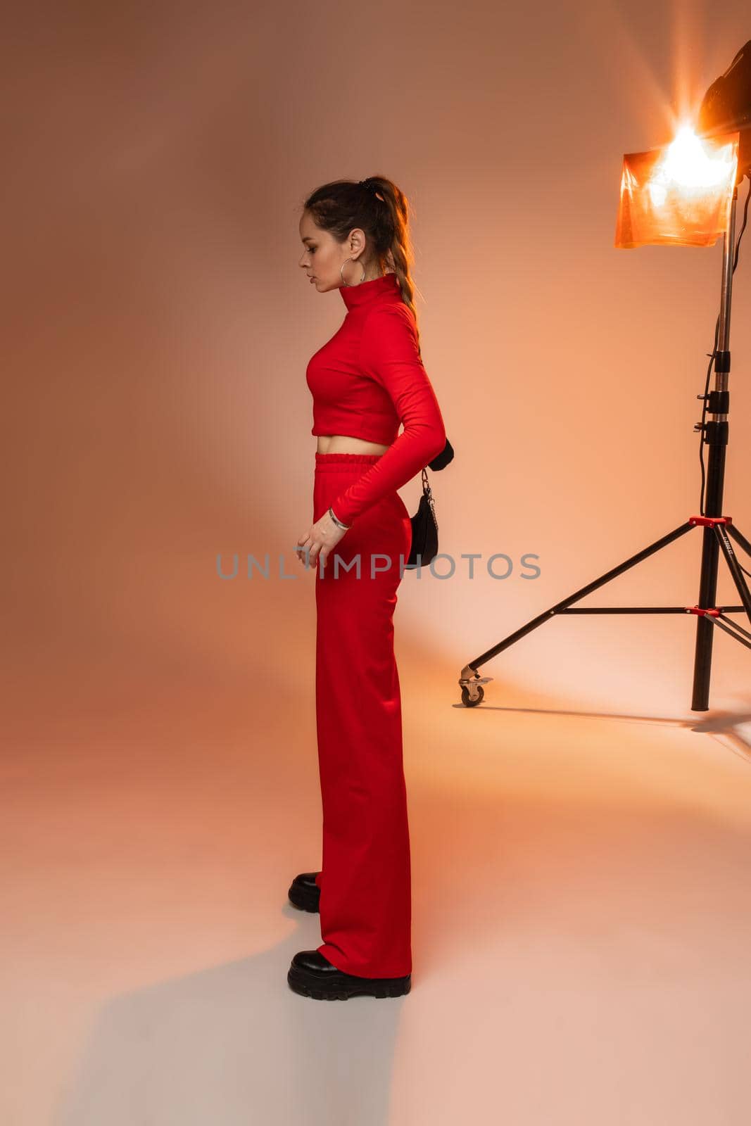 Side view of slender young woman in red suit posing in studio. Fashion and style concept