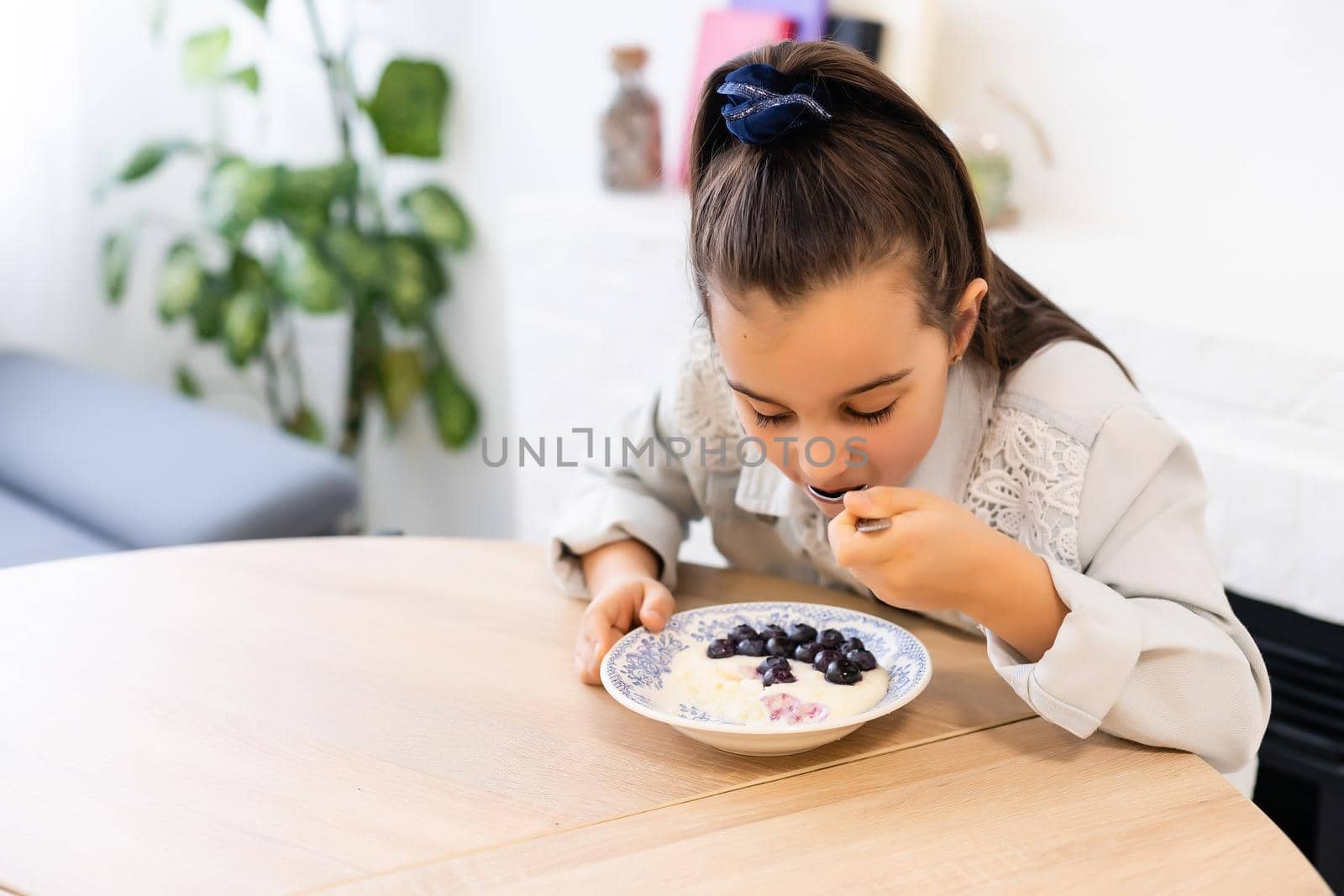 little girl eating porridge with blueberries by Andelov13