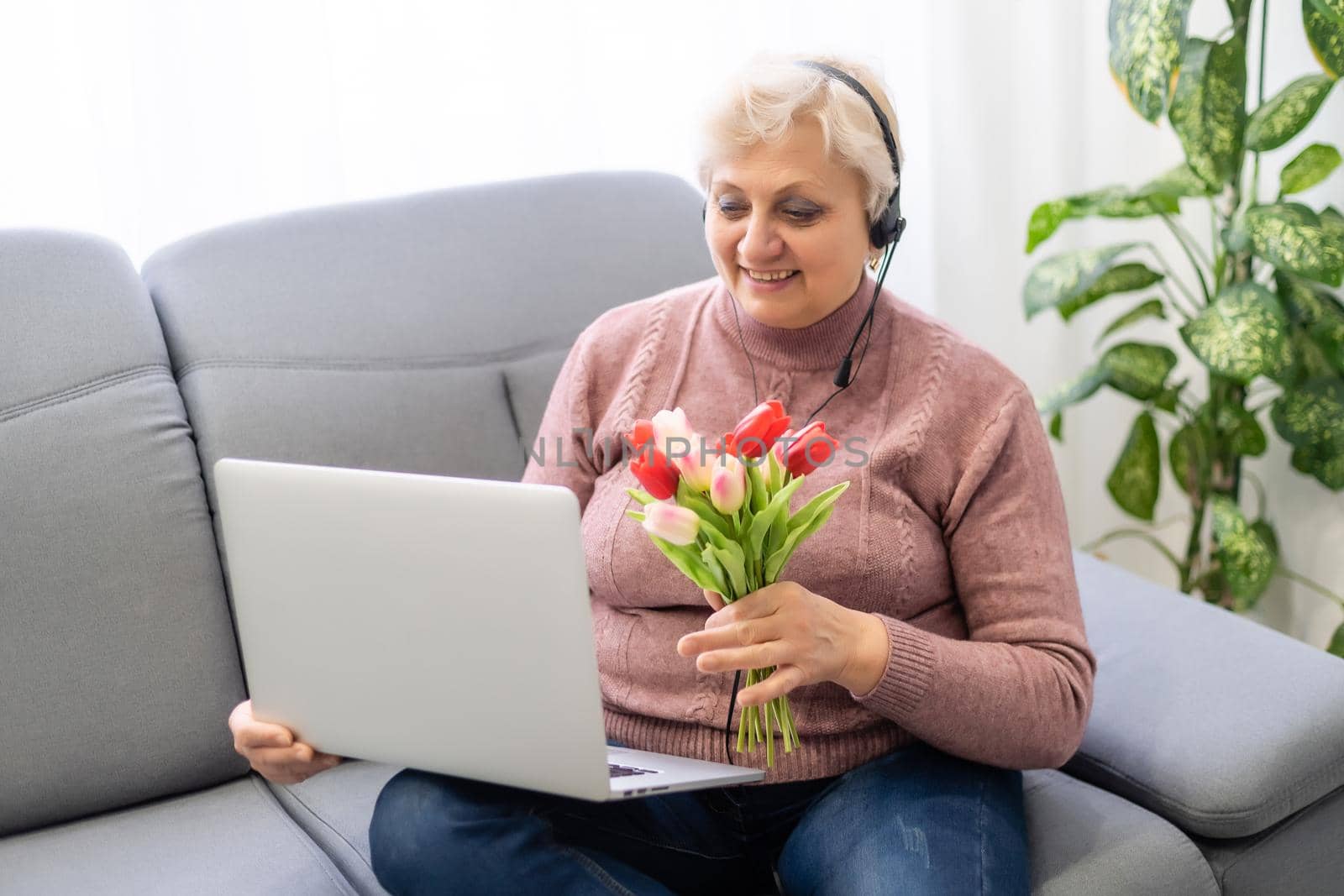 Cropped shot of a beautiful elderly woman using laptop computer while sitting with flowers.