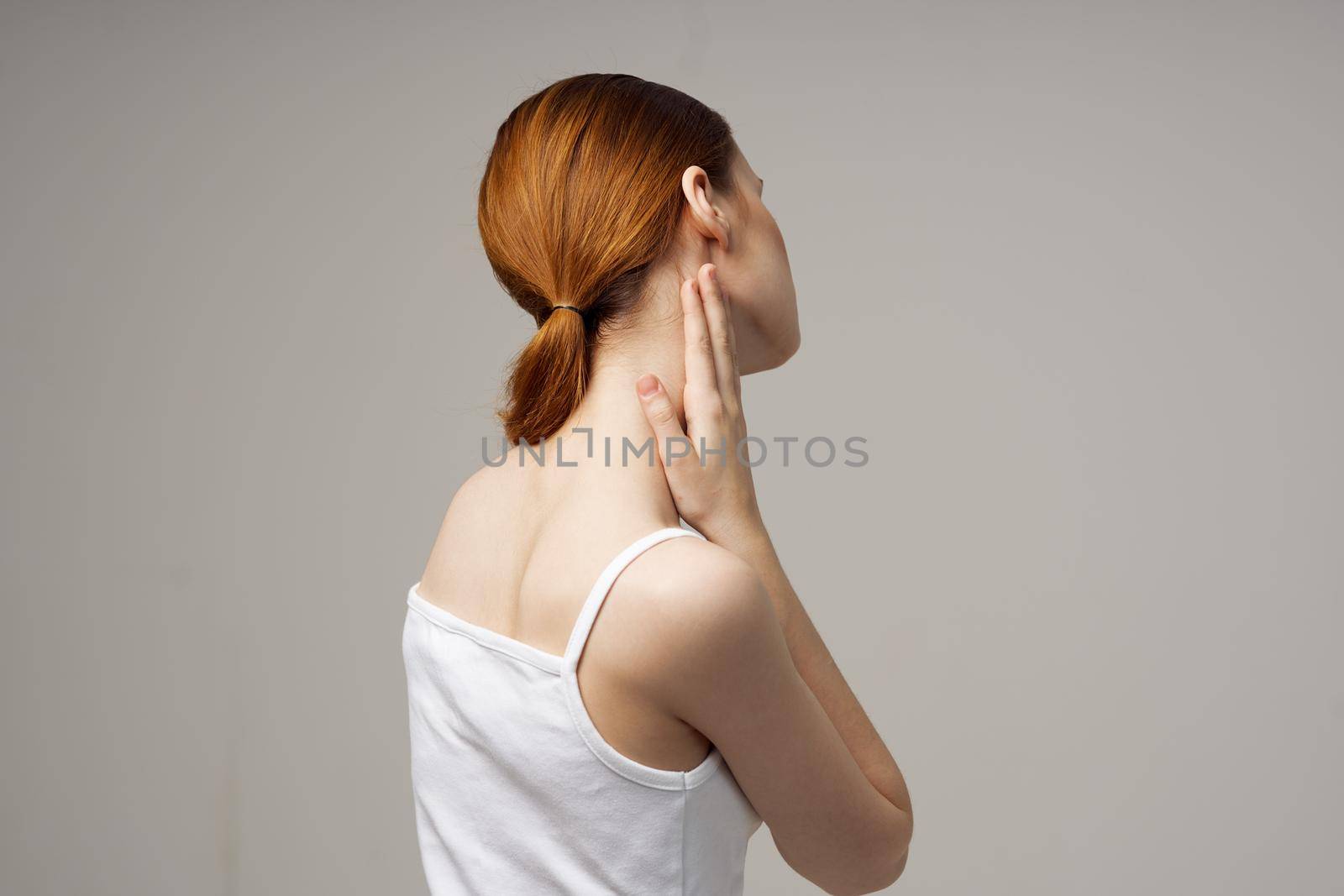 woman in white t-shirt holding on to the neck health problems joint light background. High quality photo