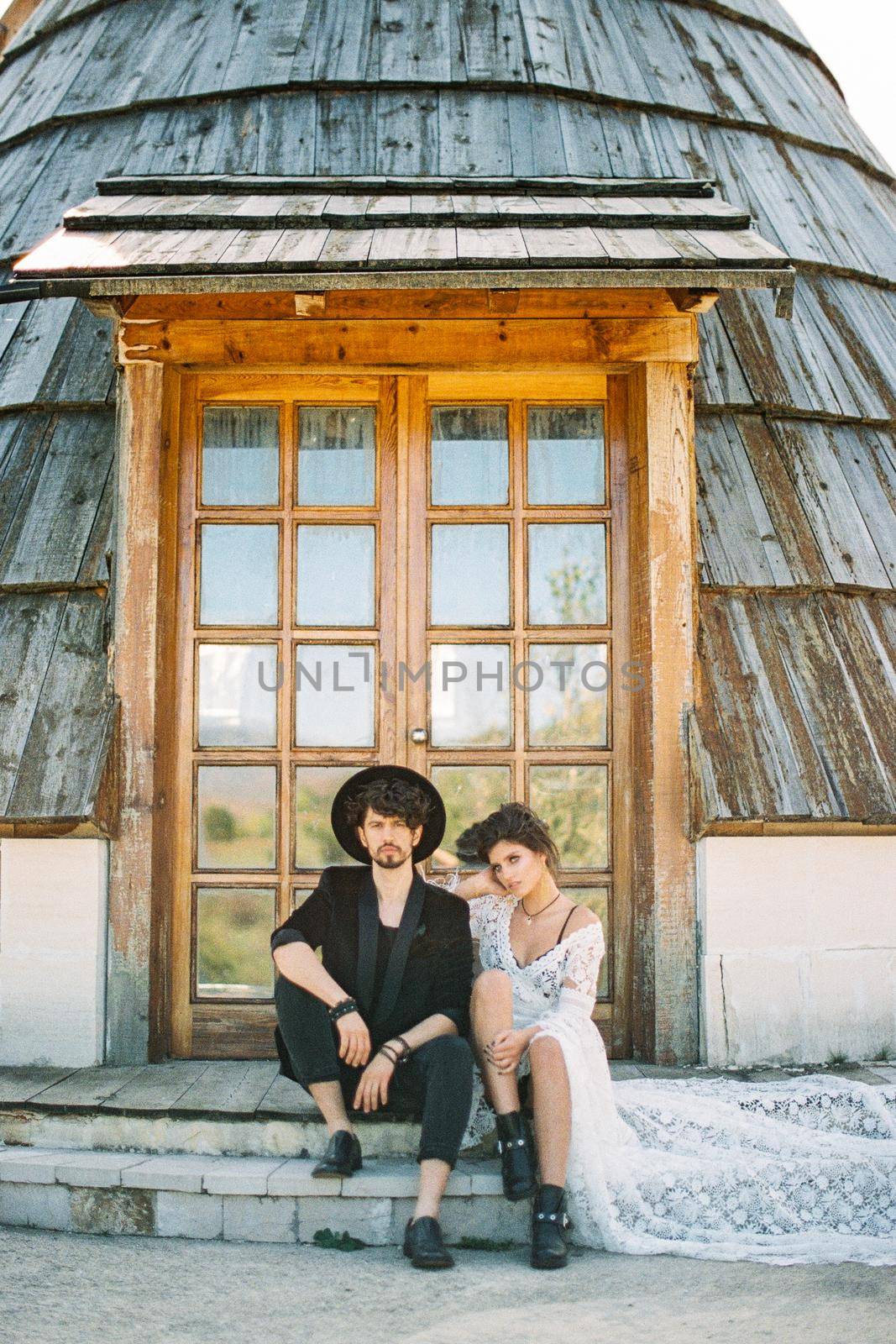 Bride and groom sit on the threshold of a wooden house. High quality photo