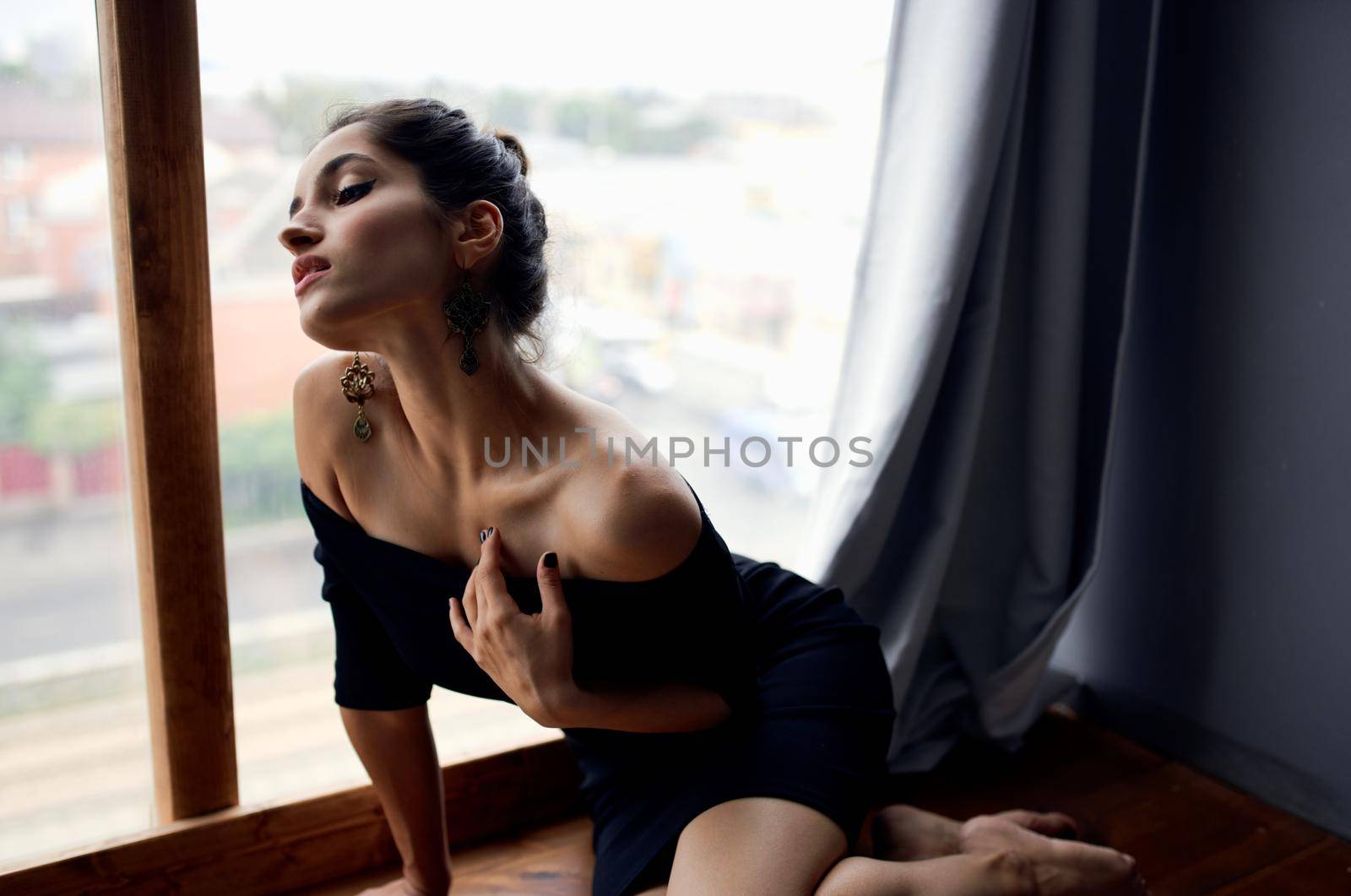 brunette in a black dress near the window posing fashion model. High quality photo
