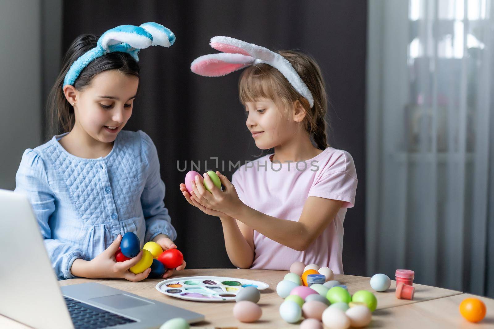 Two little cute girls with bunny ears are painting Easter eggs, children are preparing for the spring holiday, Easter mood, children are drawing on eggs. by Andelov13