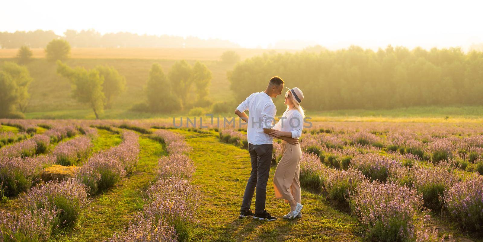 Smiling young couple embracing at the lavender field, holding hands, walking. by Andelov13